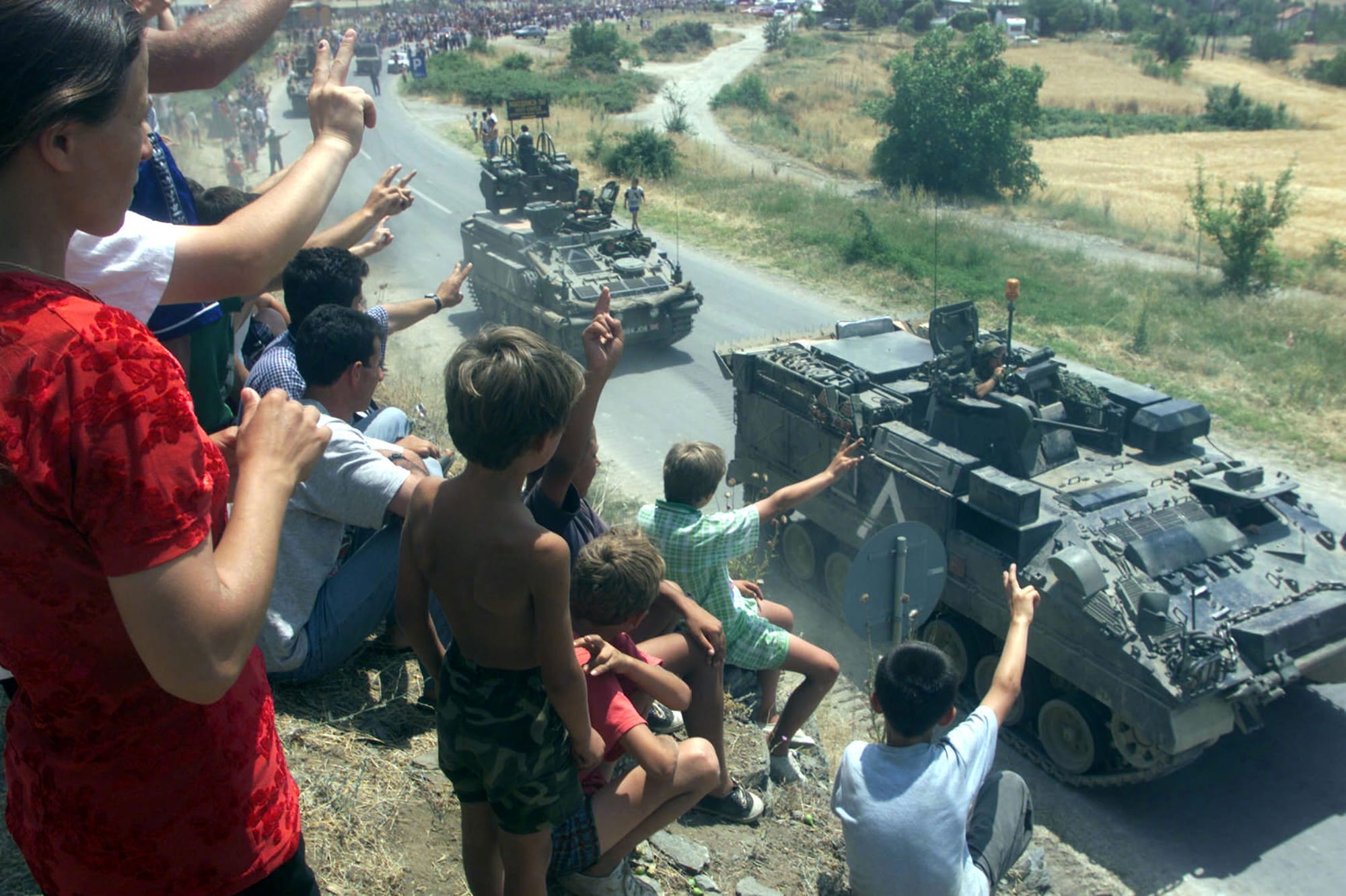 Kosovo Albanian refugees on a roadside cheering NATO armoured vehicles at the border, 1999