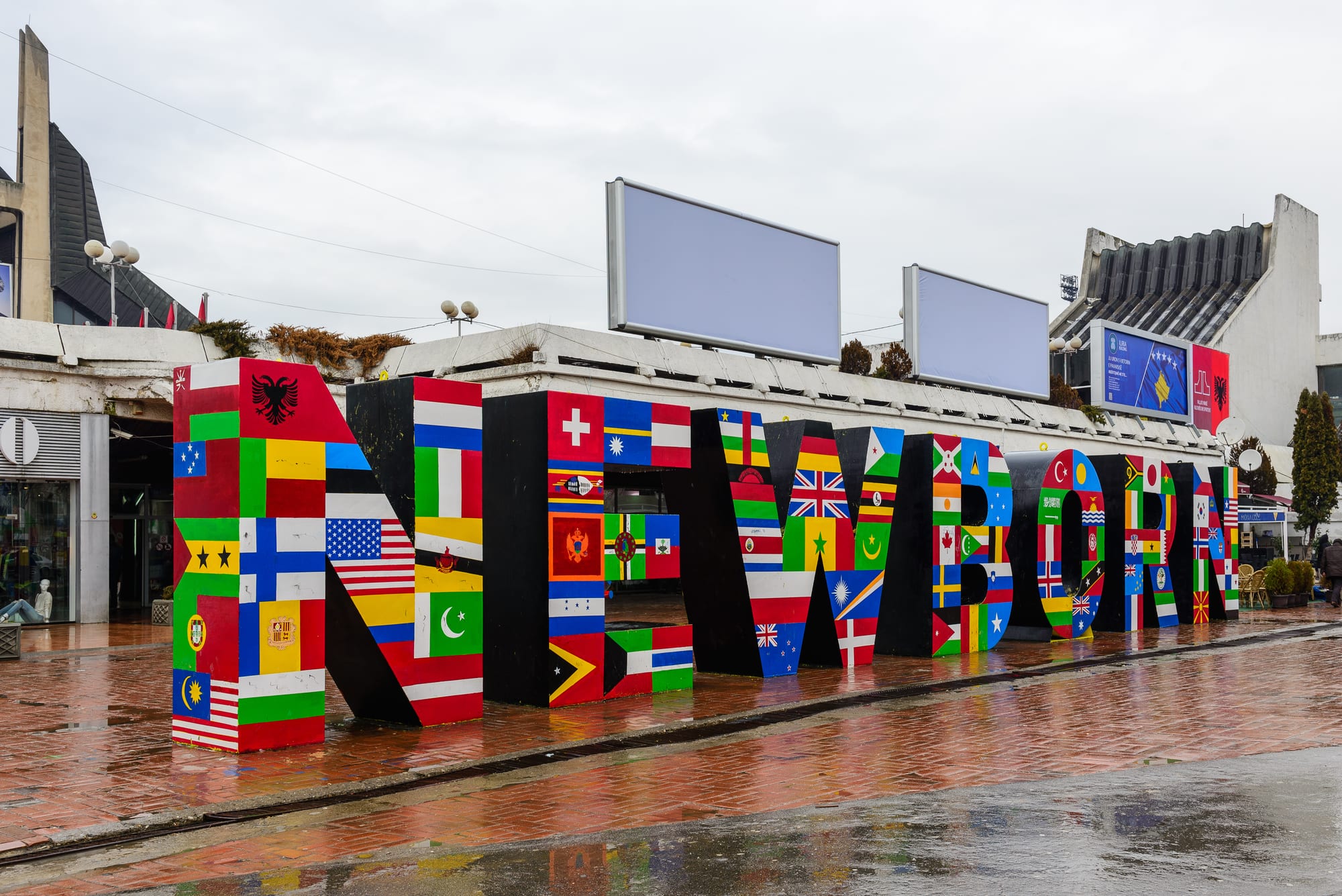 Large yellow block letters spelling NEWBORN in a Pristina square, covered in signatures