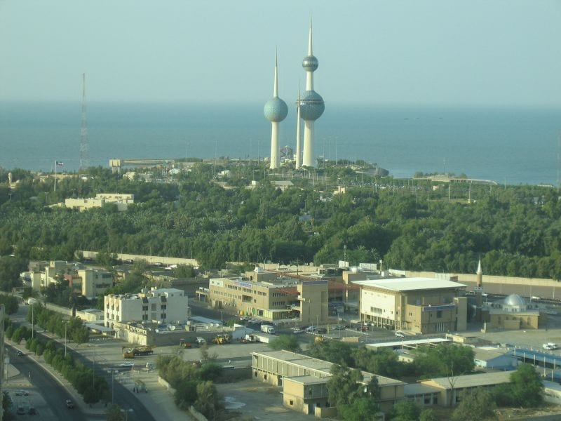 Three tapering concrete towers, two topped with blue-green spheres, against a clear sky by the sea