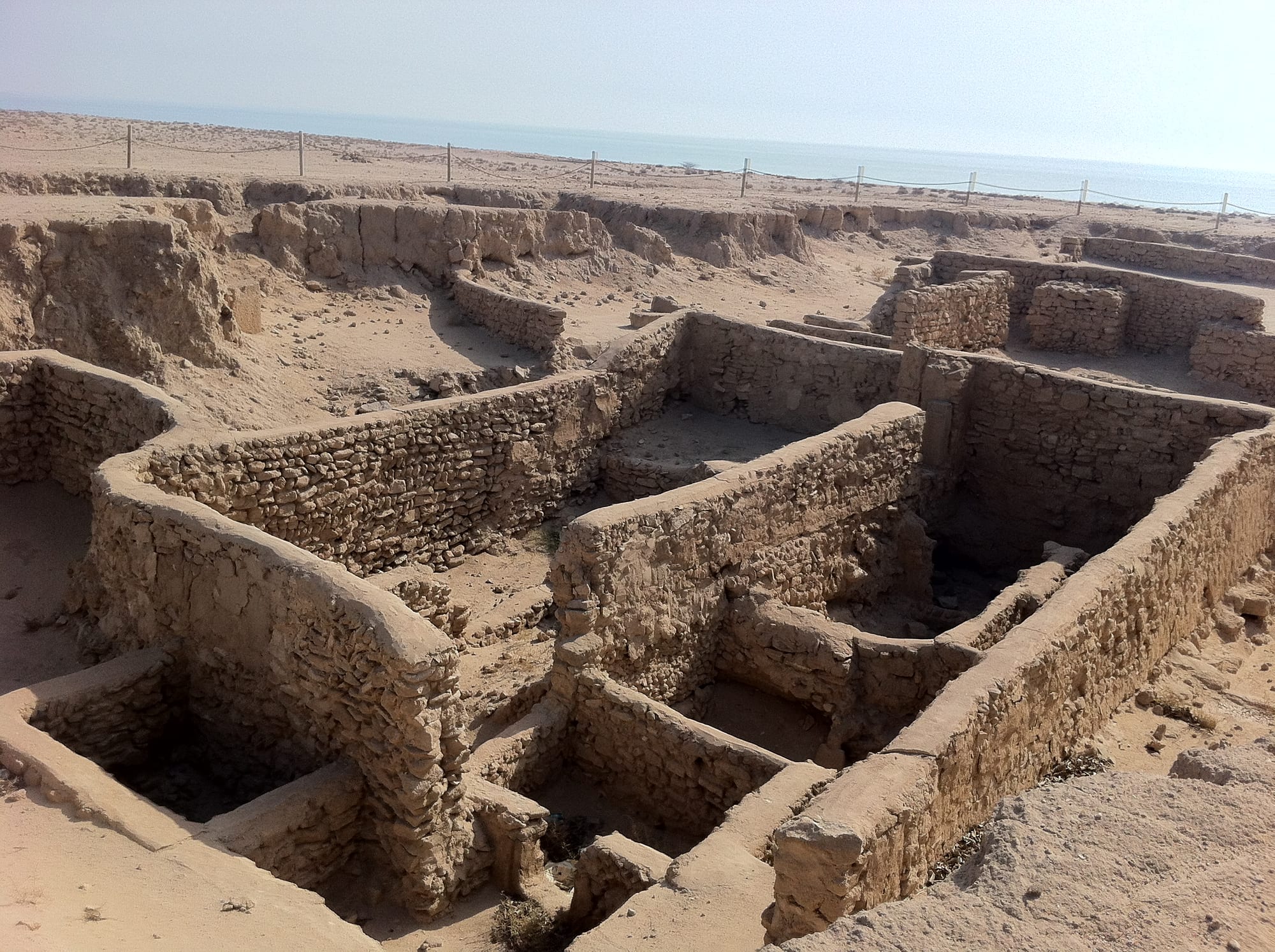 Excavated low stone walls and foundations of an ancient settlement above the sea