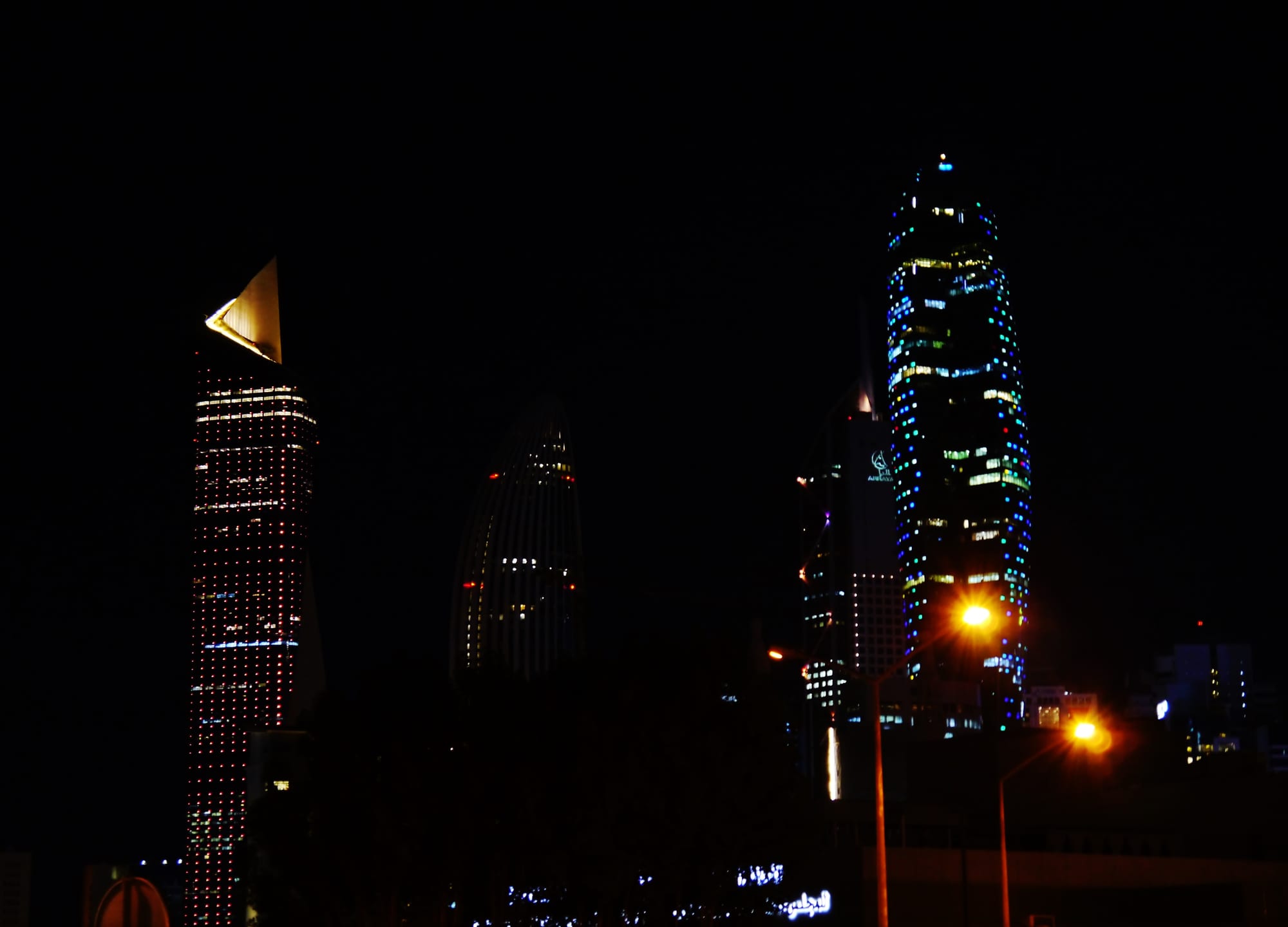 A row of illuminated glass skyscrapers along a waterfront at night