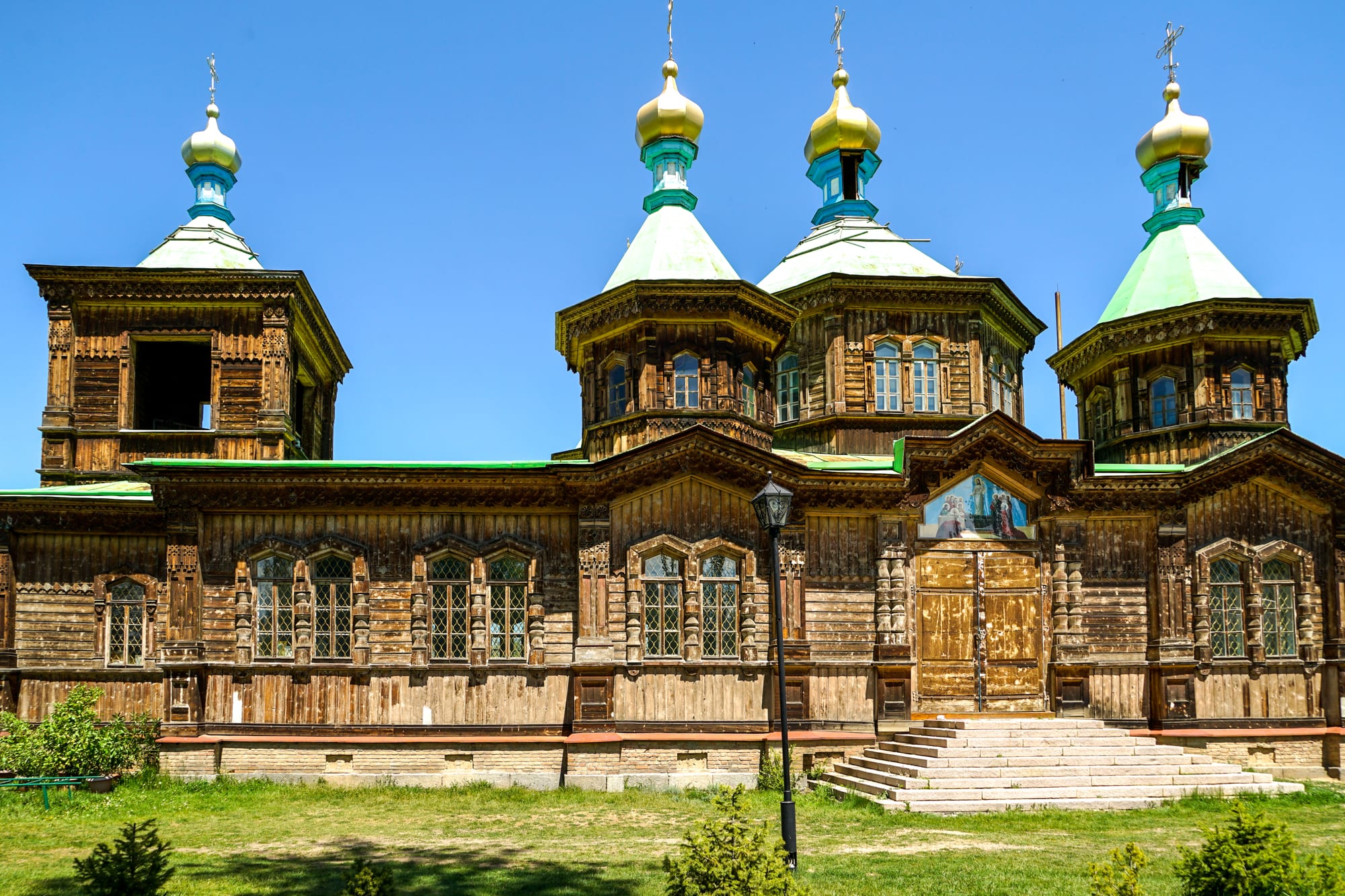 A wooden Orthodox church with a green roof and onion domes among trees