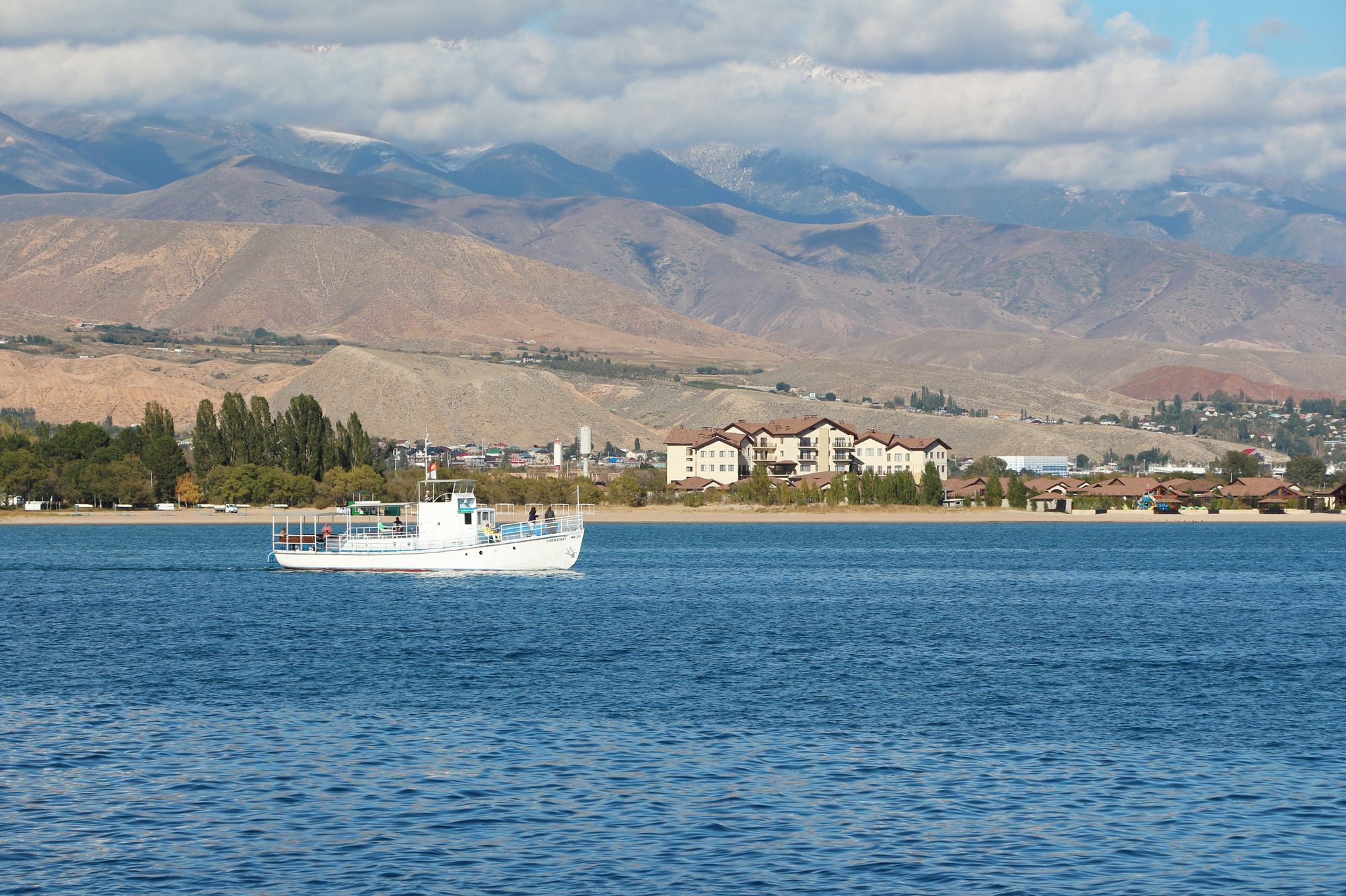 A vast blue lake meeting a beach, with a wall of snow-capped mountains along the far shore