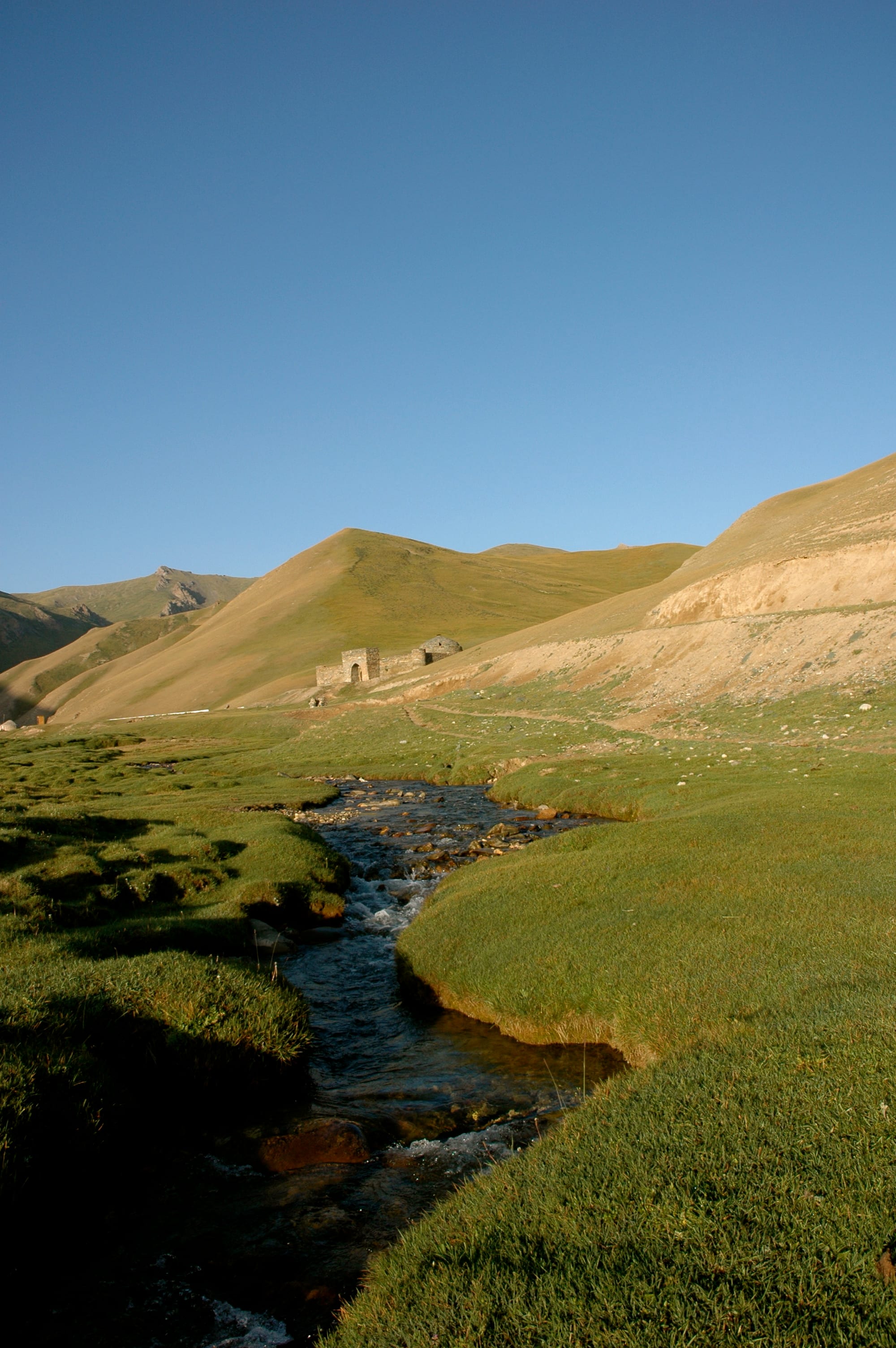 A low stone building with a domed roof half-buried in a grassy mountain valley
