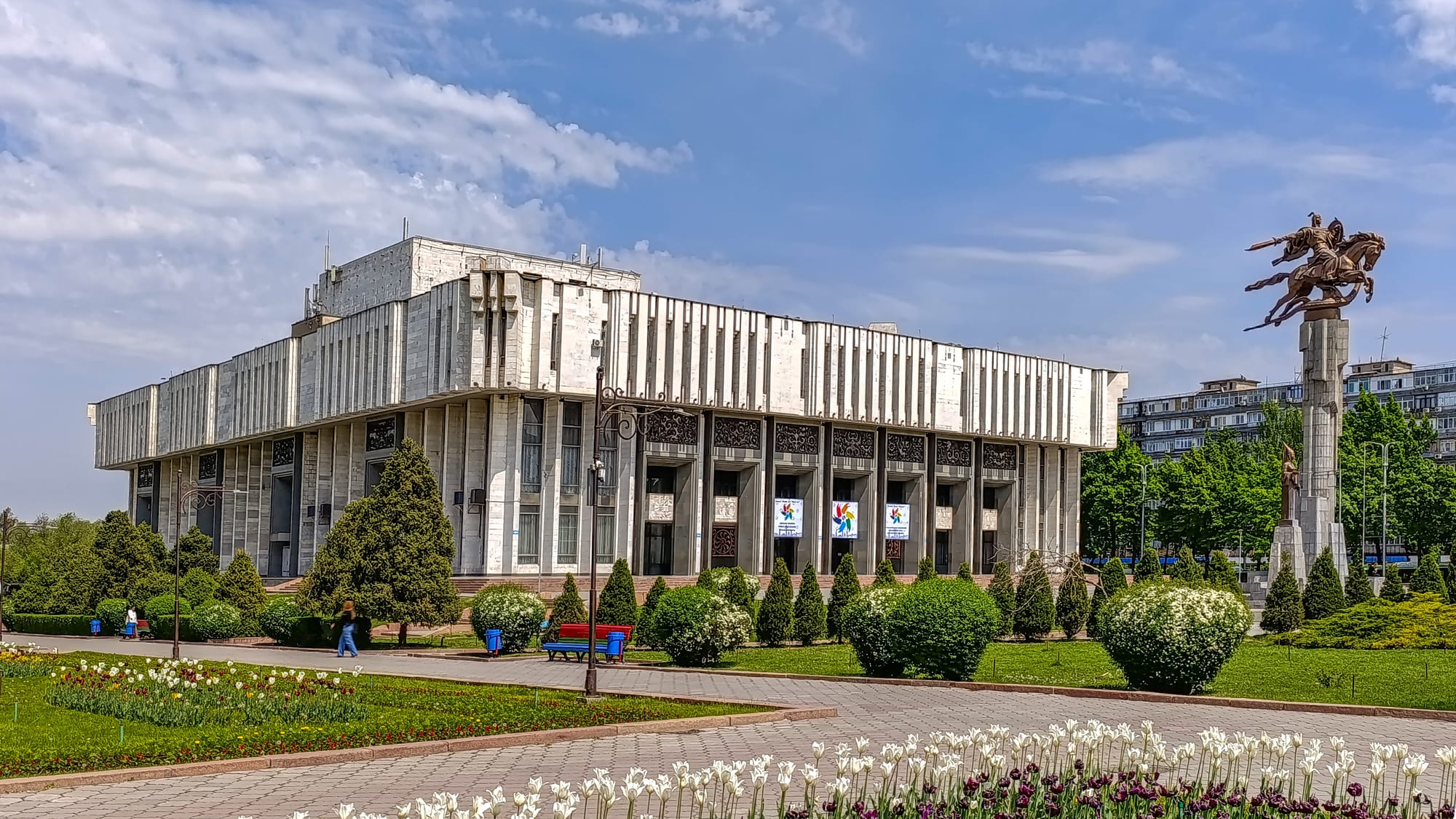 An equestrian statue of the hero Manas in front of a large concert hall in Bishkek
