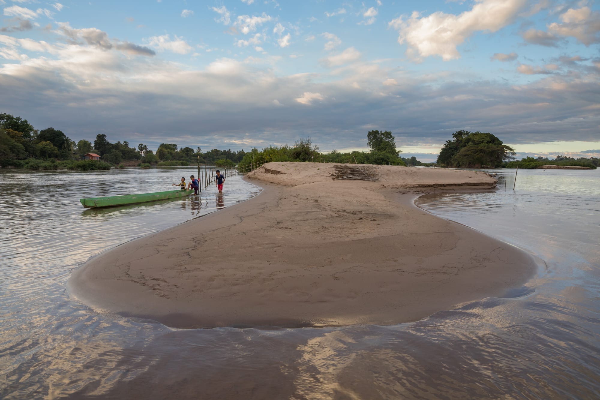 A wide, calm stretch of the Mekong river with a sandy beach and small boats