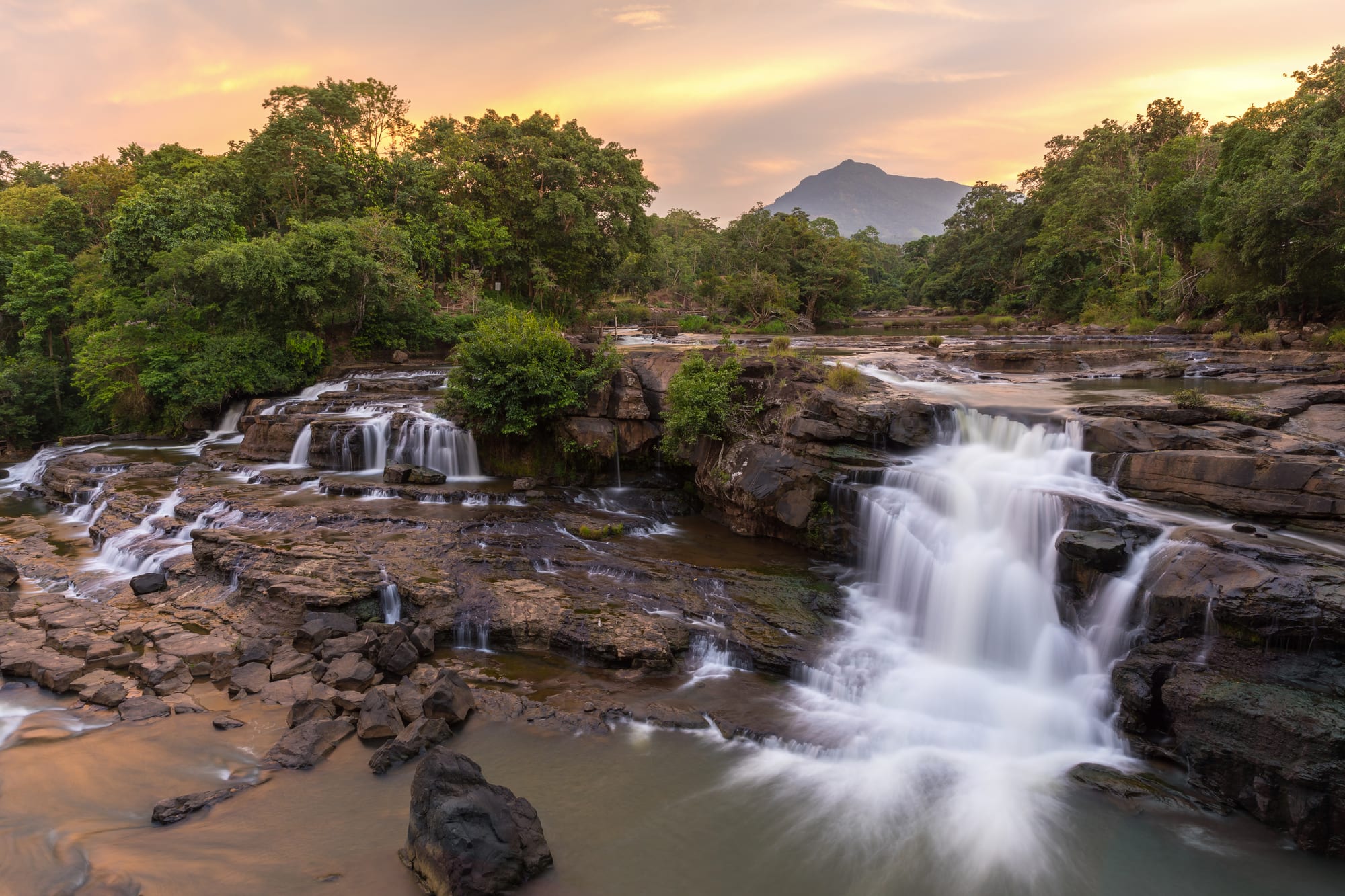 A broad waterfall spilling over a wide rock ledge into a river at sunset