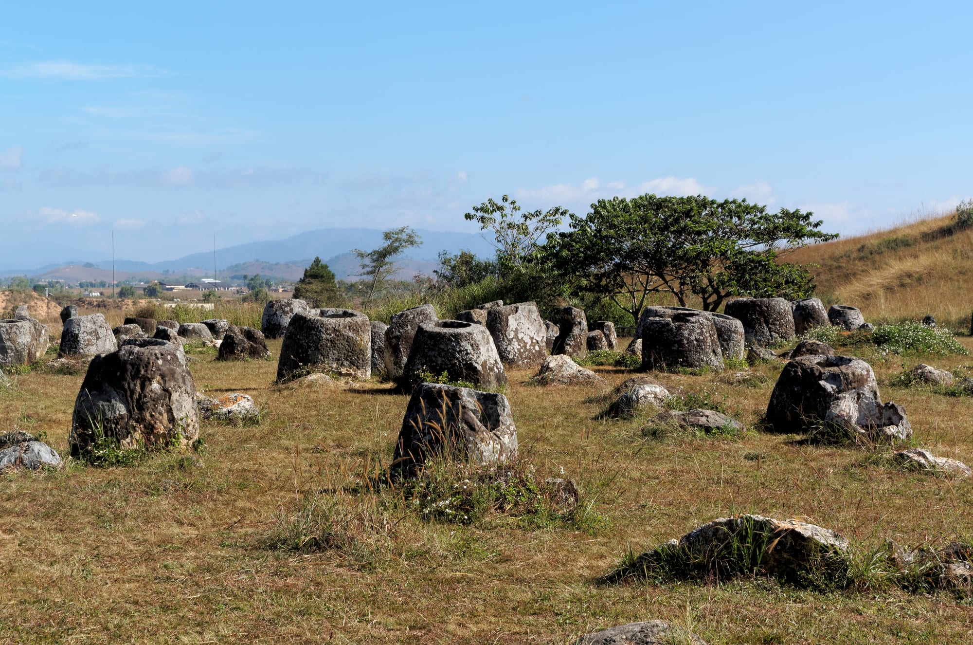 Dozens of large, weathered stone jars scattered across grassy open ground