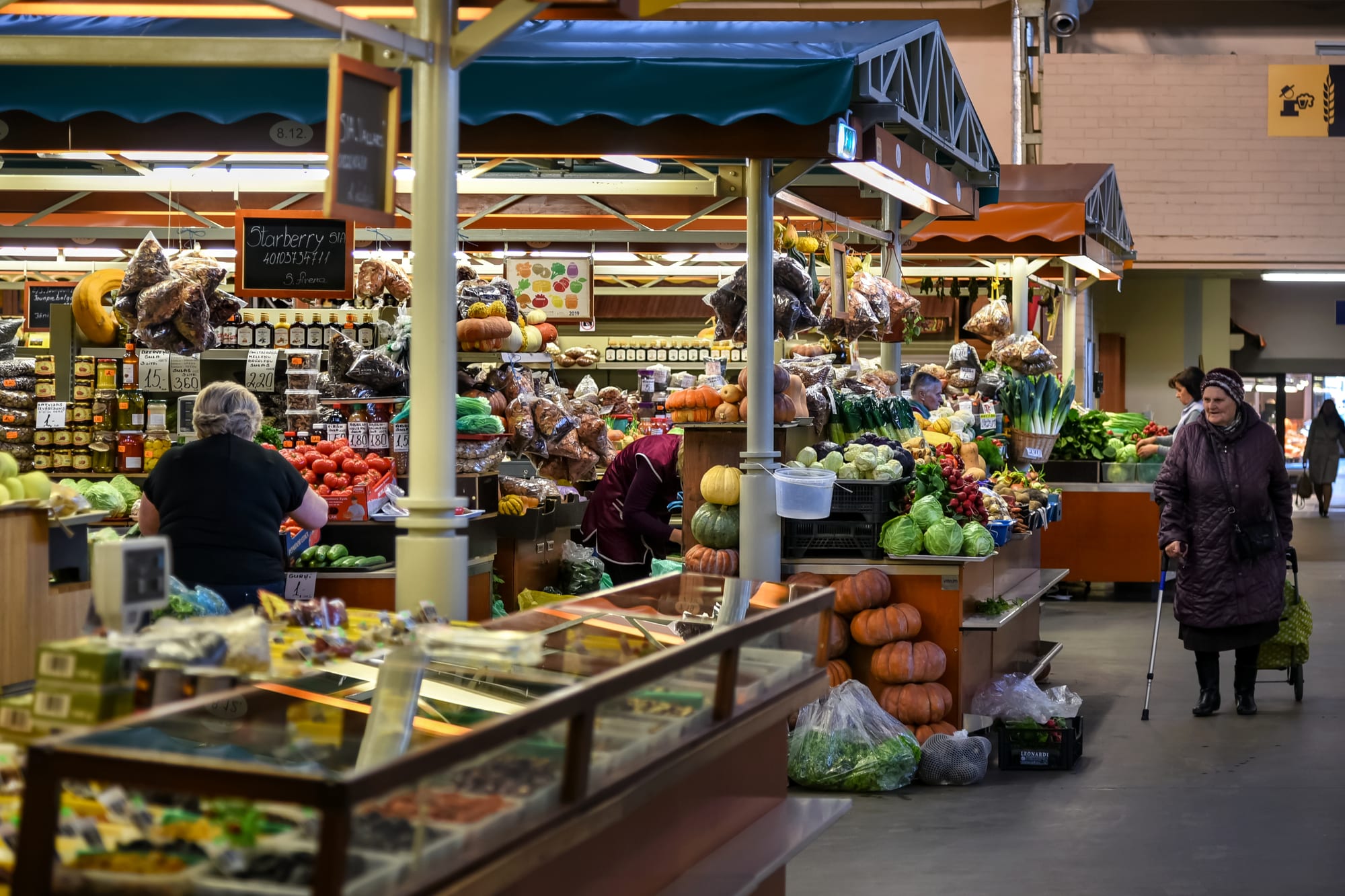 Shoppers browsing stalls of fresh vegetables, pumpkins and preserves inside a covered market hall