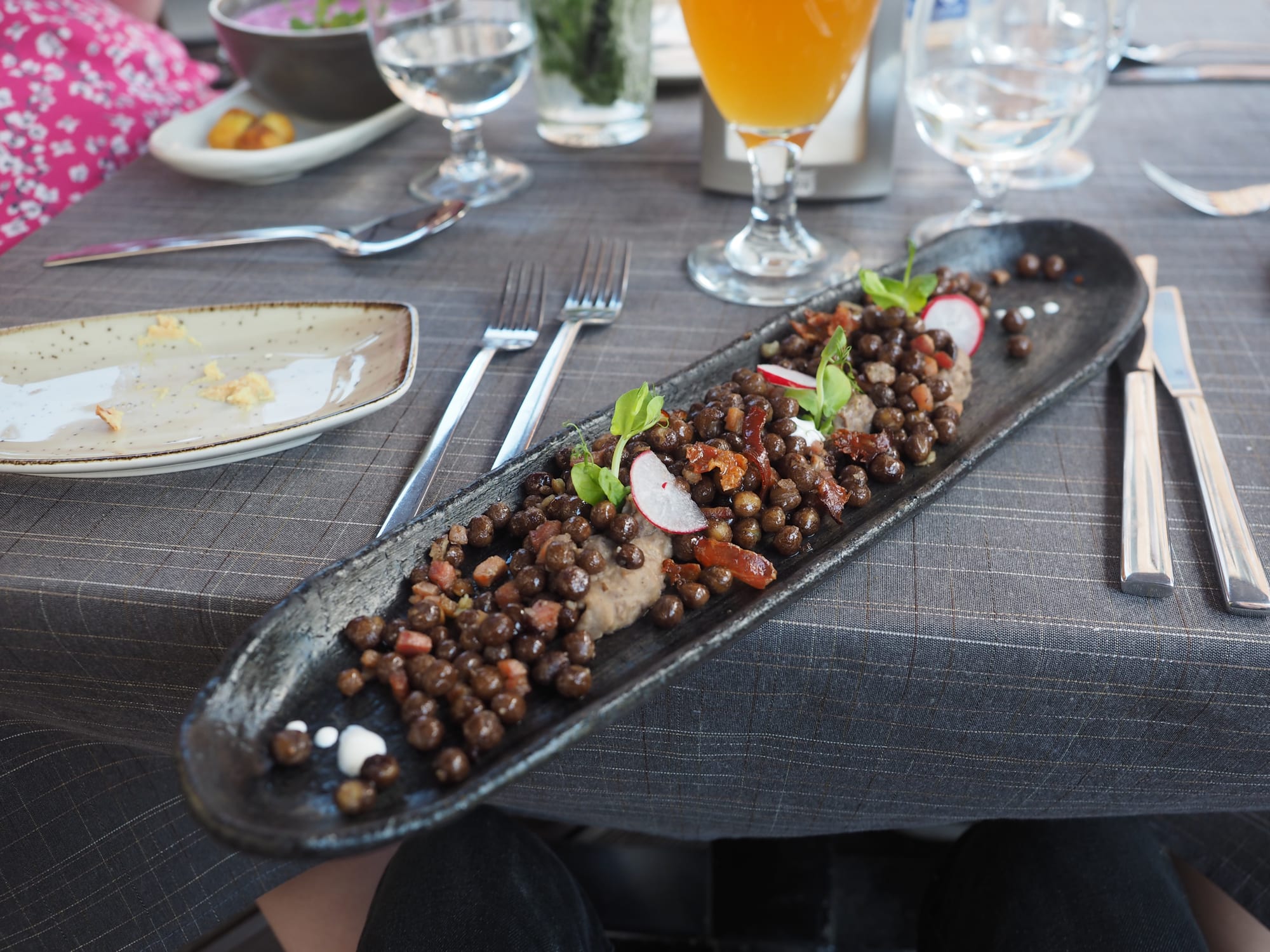 A plate of grey peas served with pieces of bacon and vegetables