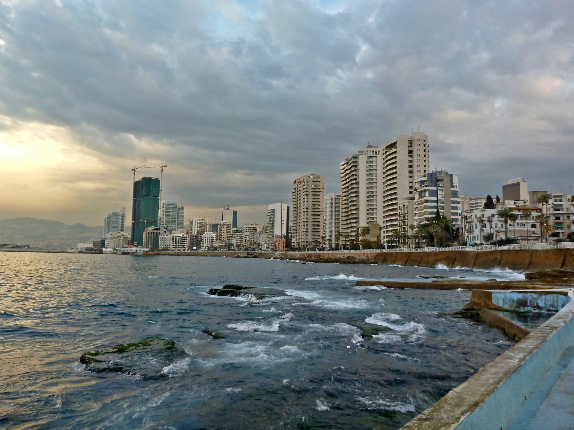A coastal city skyline of high-rise towers seen from a seafront promenade at dusk