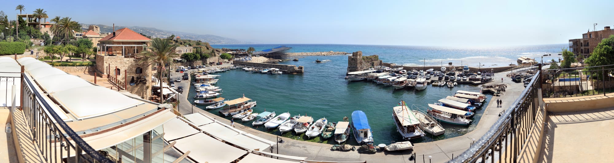 A small stone harbour with fishing boats, ancient ruins visible on the point beyond