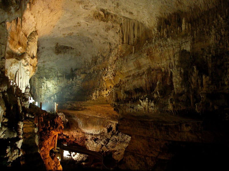 A vast illuminated cave chamber with tall stalactites and walkways