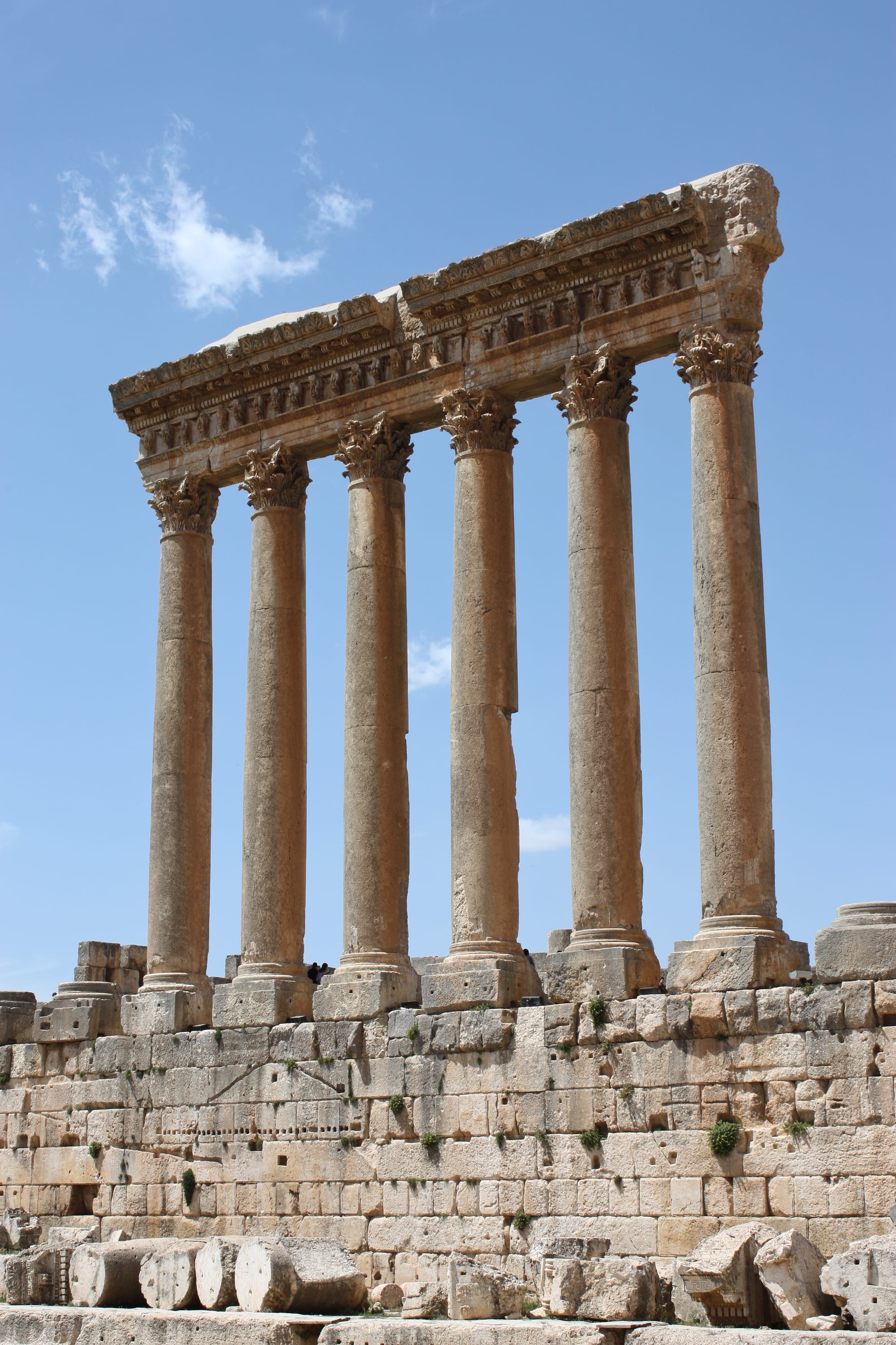 Six giant stone columns standing in a row against the sky, ruins around them