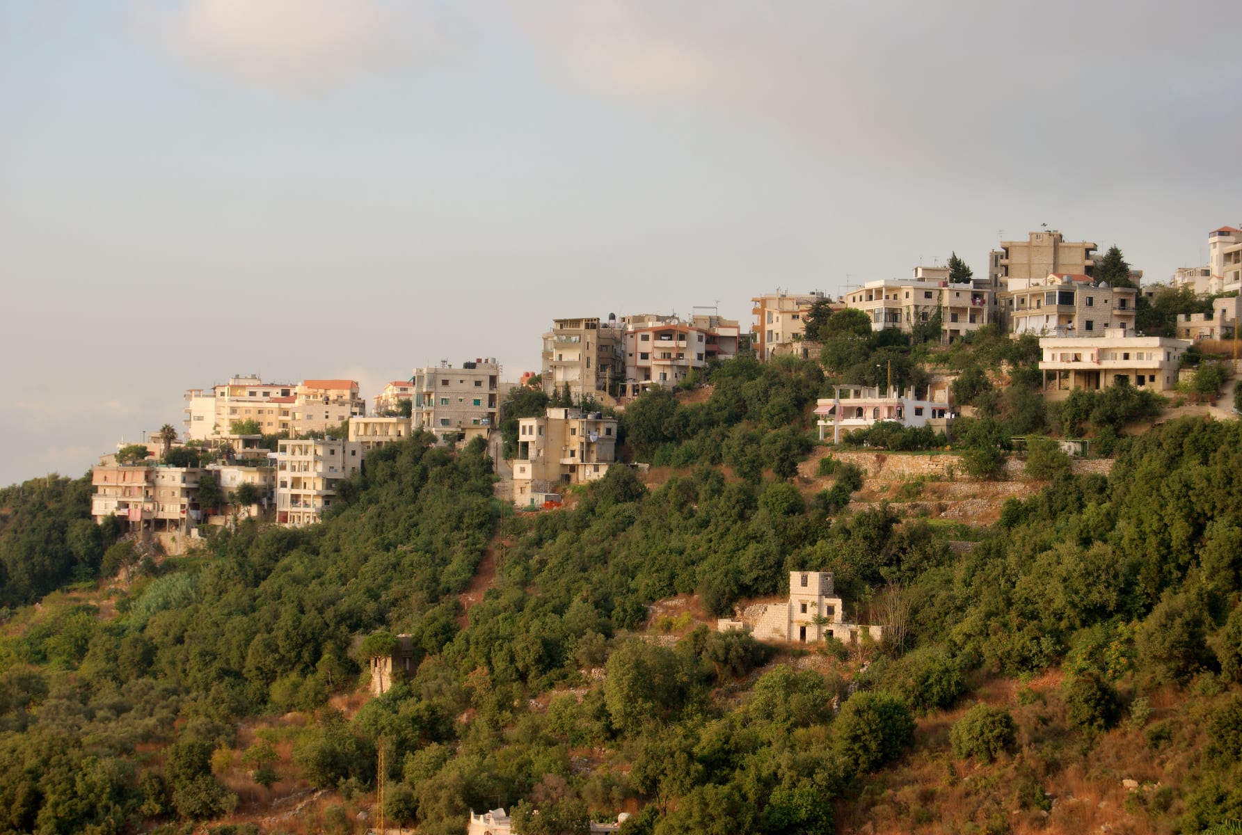 Multi-storey houses and apartment buildings clustered along a green, terraced hillside in the mountains above Beirut