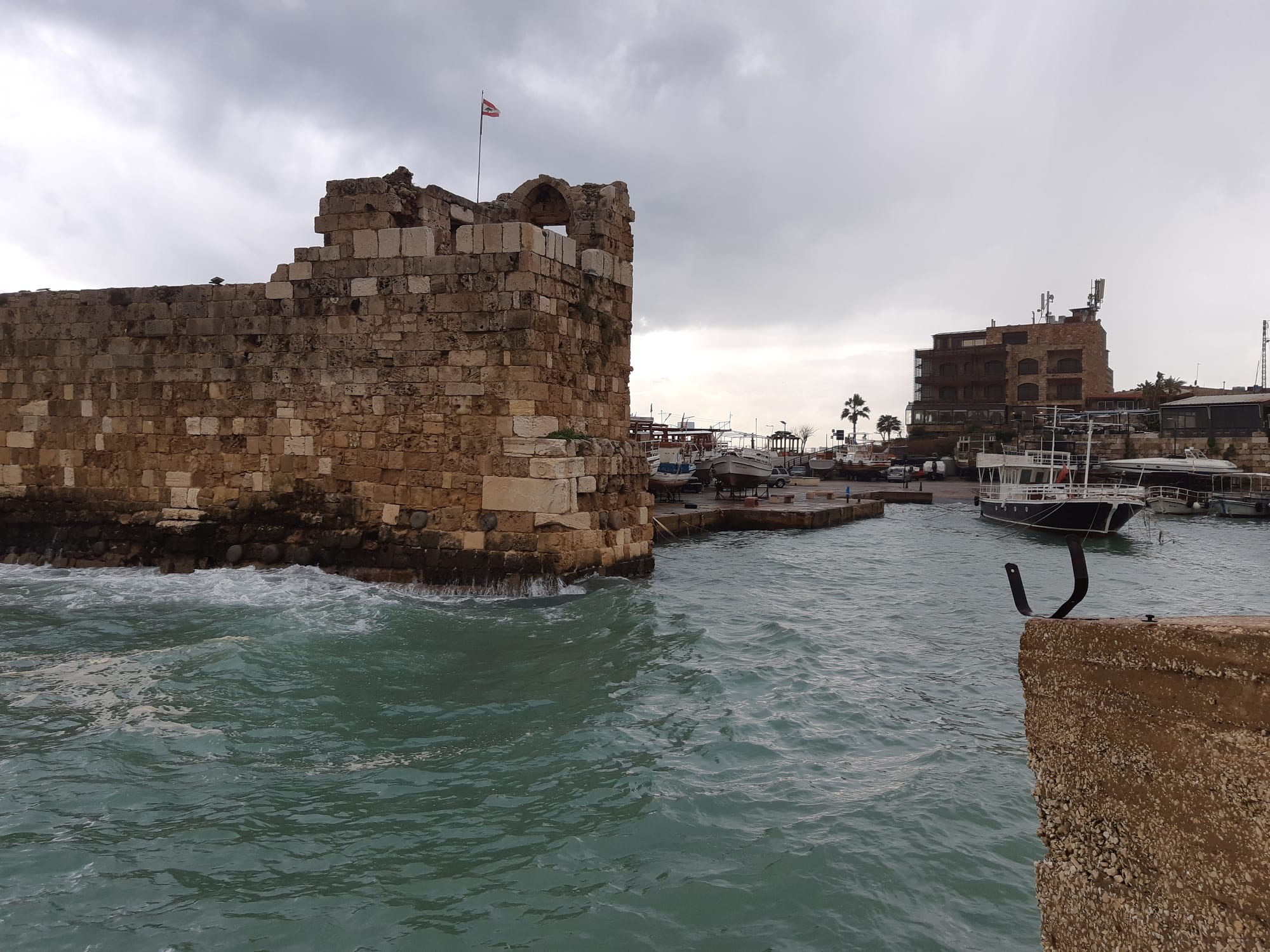 A small stone-walled harbour with fishing boats below an old town and a medieval castle