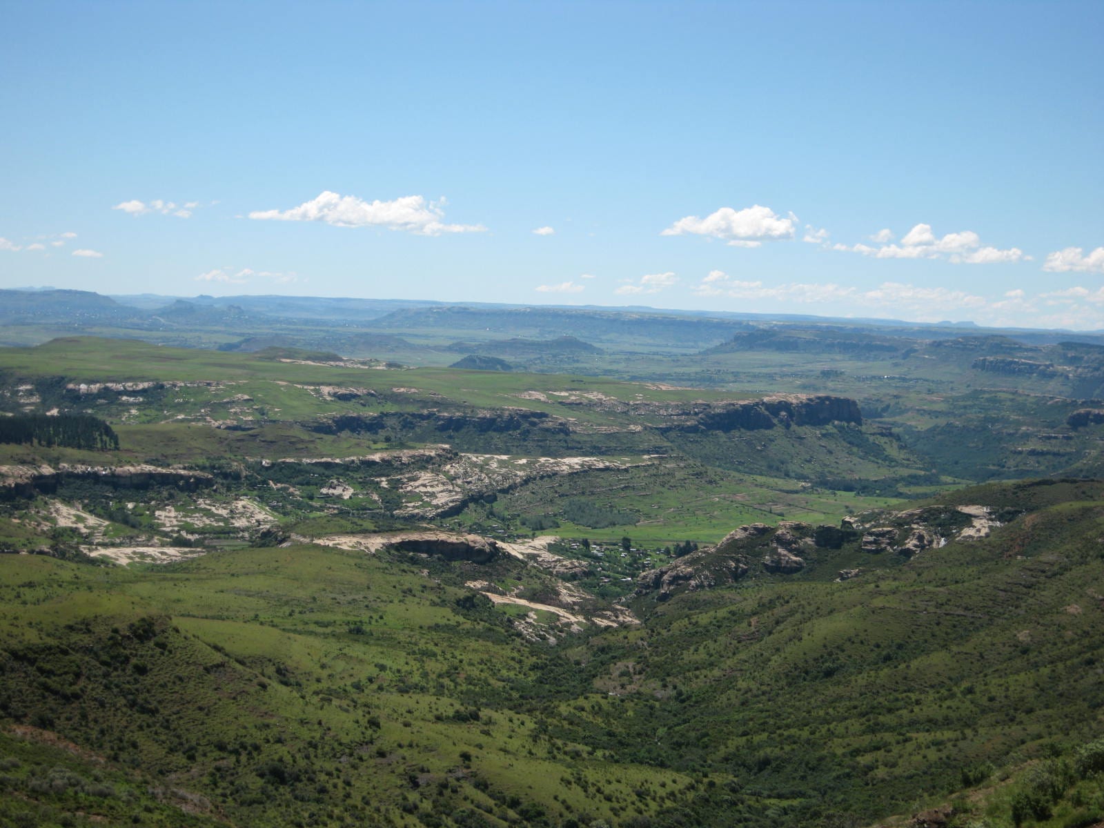 A wide green valley of farmland and scattered villages below sandstone cliffs