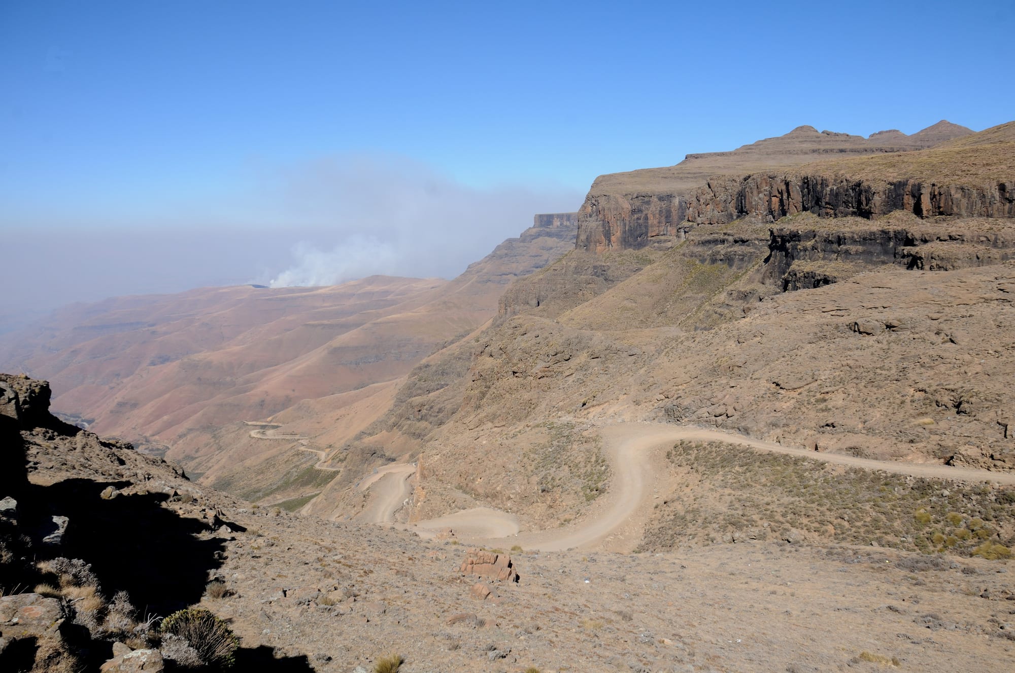 A gravel mountain road switchbacking steeply up a highland escarpment