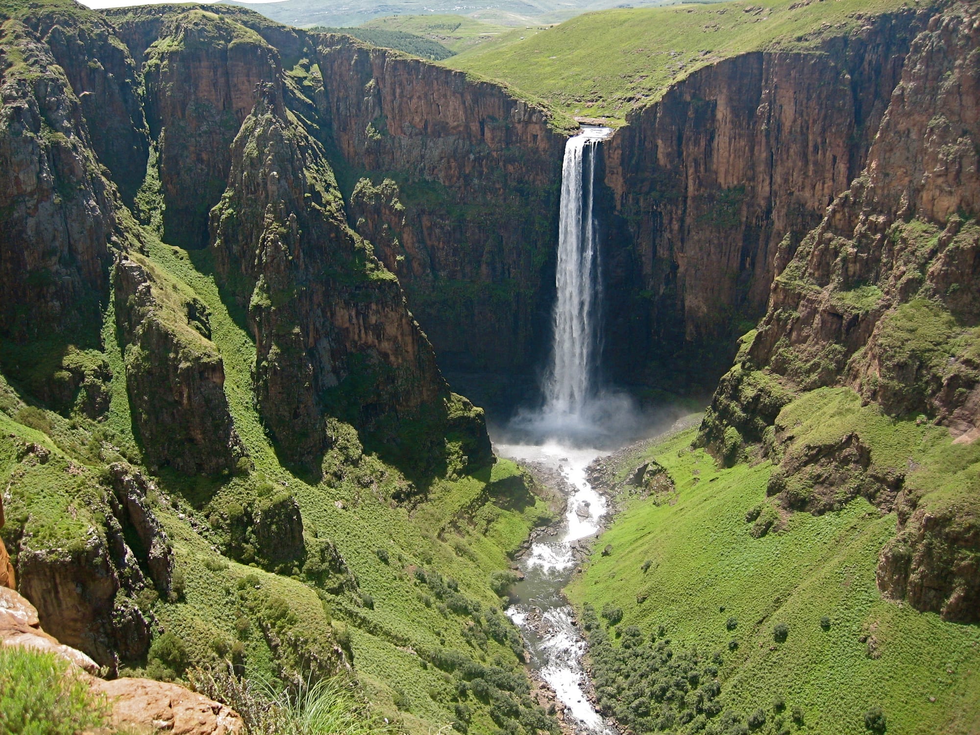 A tall single-drop waterfall pouring into a deep rocky gorge, seen from above