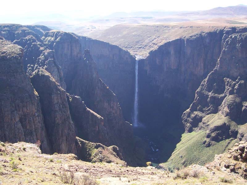 A single tall waterfall plunging off a cliff edge into a rocky highland gorge