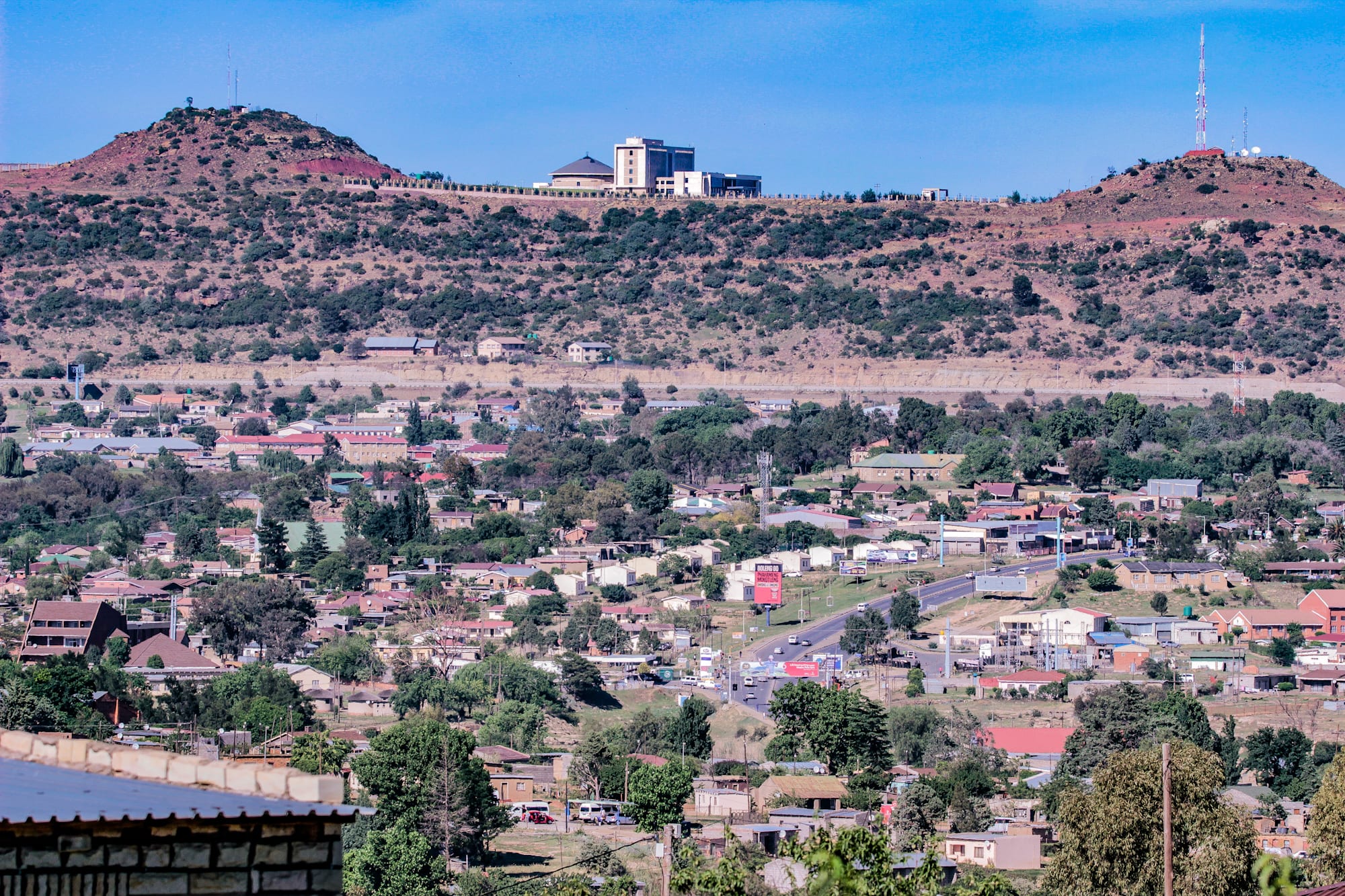 A wide view of Maseru, Lesotho's capital, with low-rise buildings, roads and trees spread across a valley below dry hills