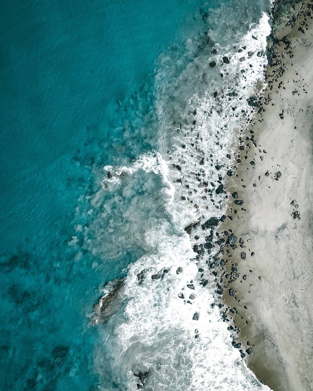 A long empty beach with rolling surf and green headlands under a bright sky