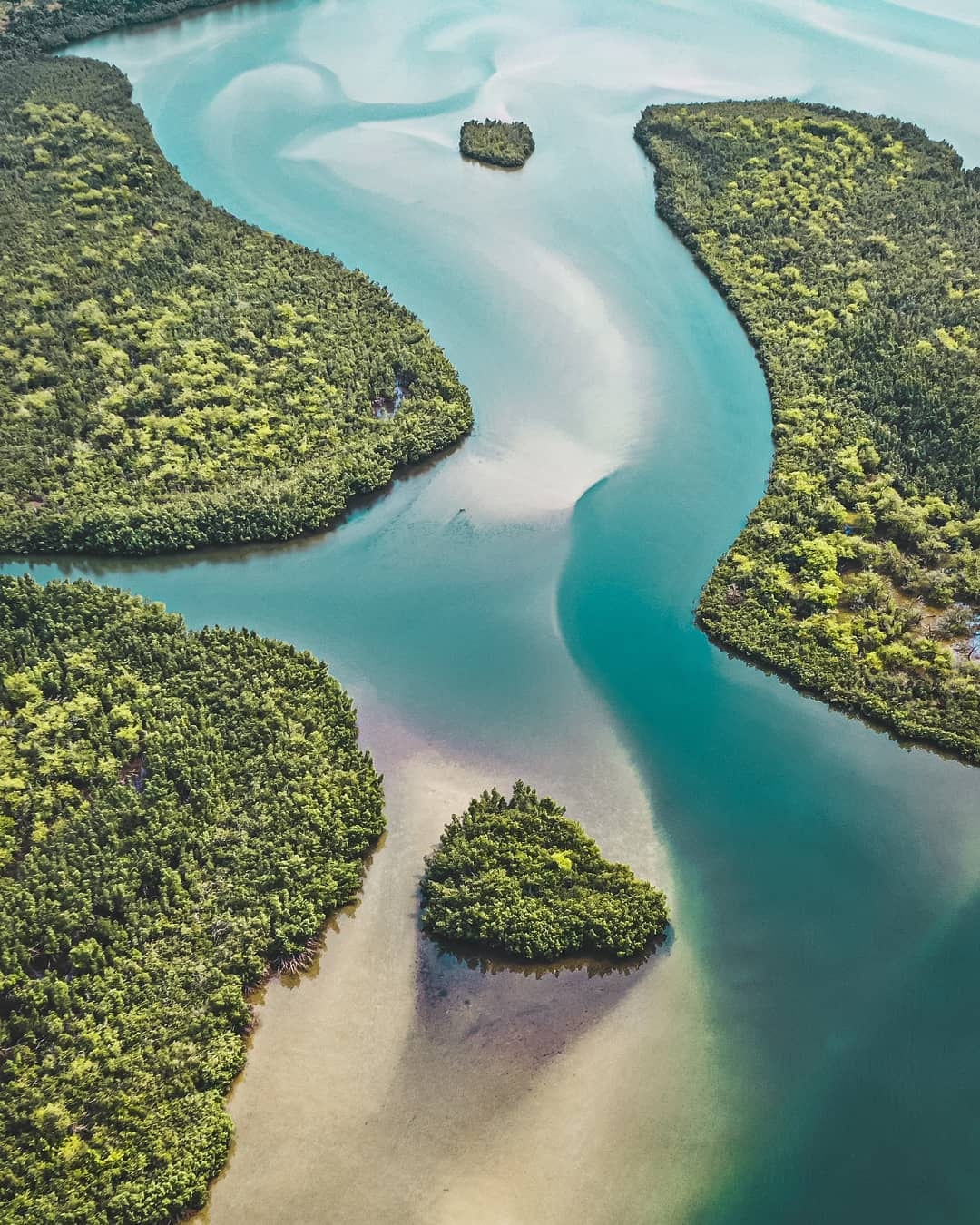A calm wide lagoon fringed by palm trees and low green hills