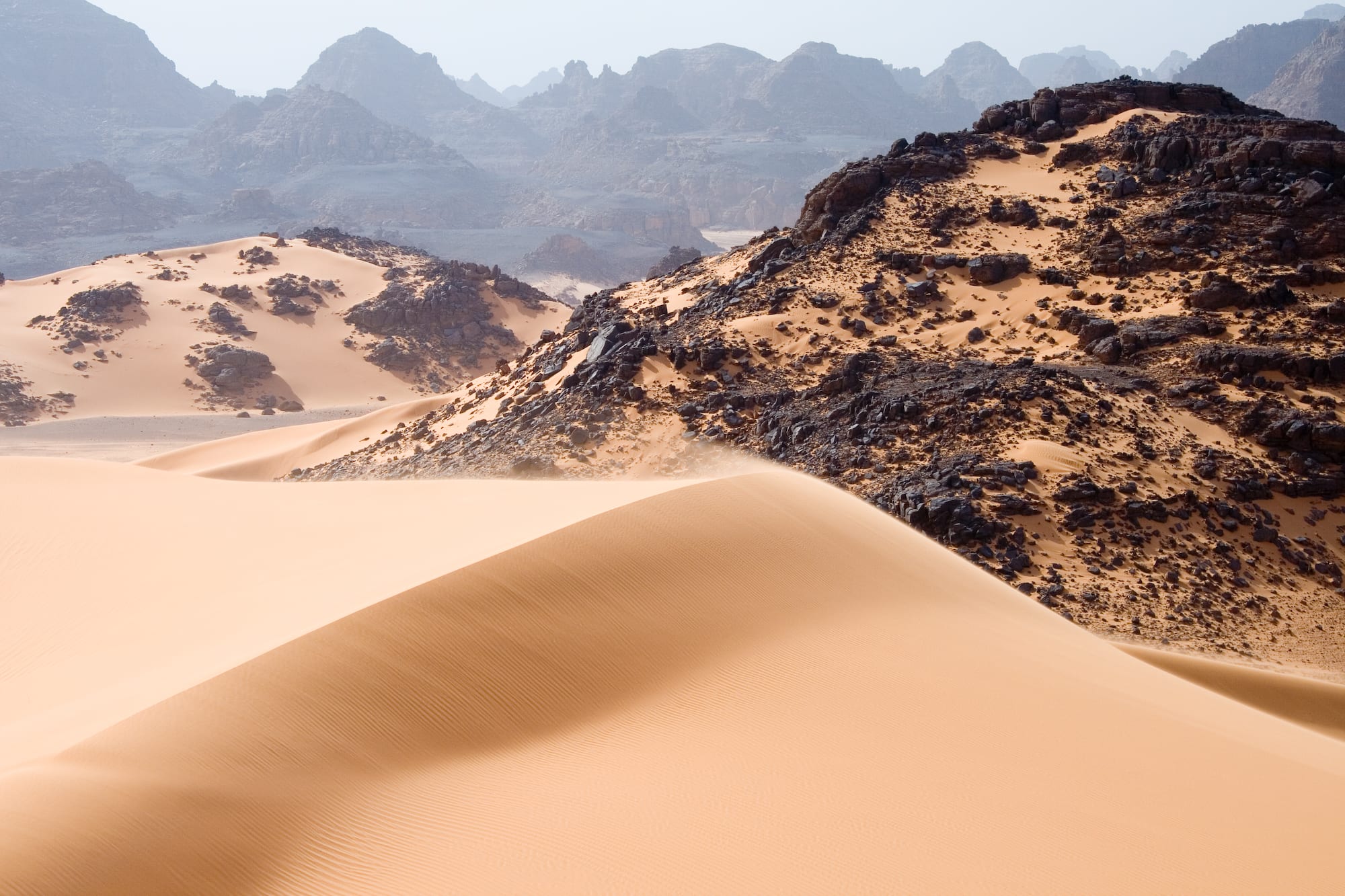 Dramatic red-orange sandstone rock formations and arches in a Saharan desert landscape