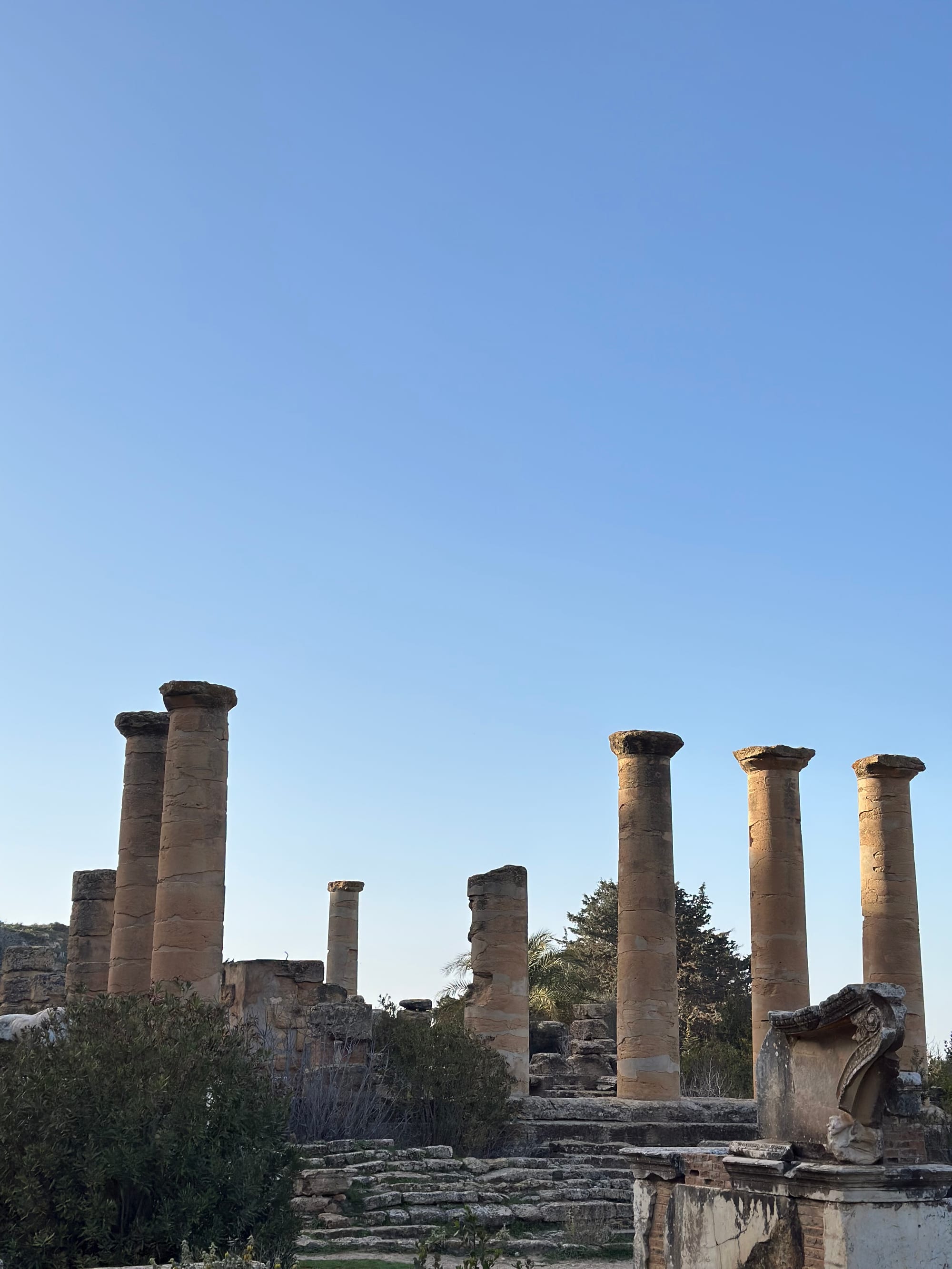 Ruined classical temple columns and terraces on a hillside overlooking green countryside