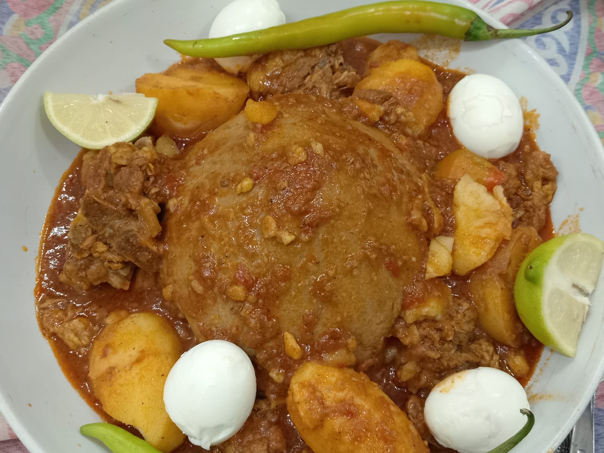 A dome-shaped dough surrounded by a red sauce and eggs on a large plate
