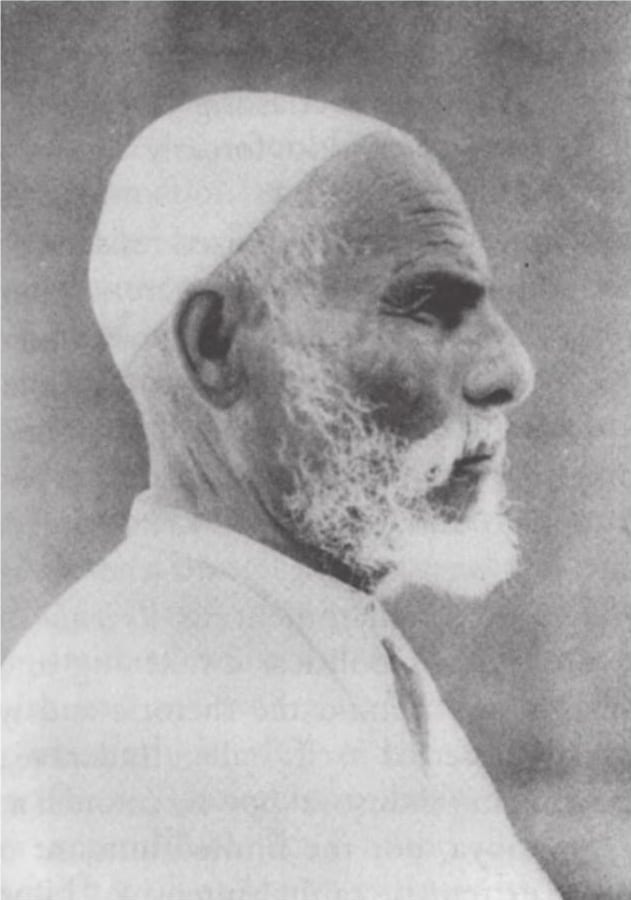 Omar Mukhtar, an elderly bearded man in robes and chains, photographed after his capture