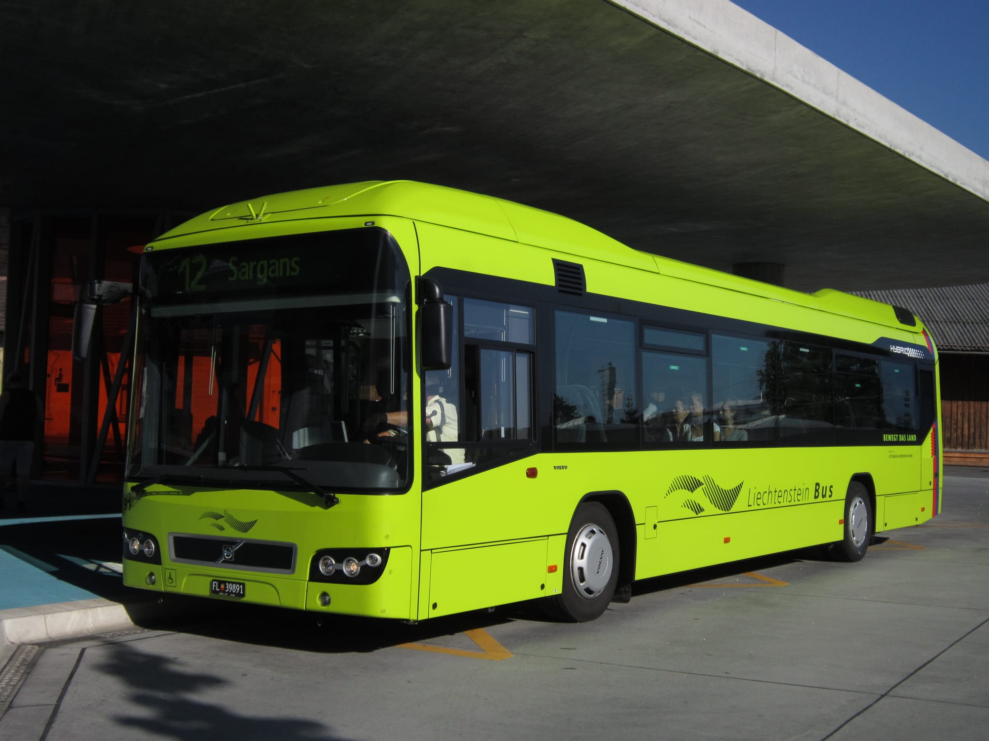 A bright green hybrid bus marked route 12 to Sargans, waiting at a covered bus stop