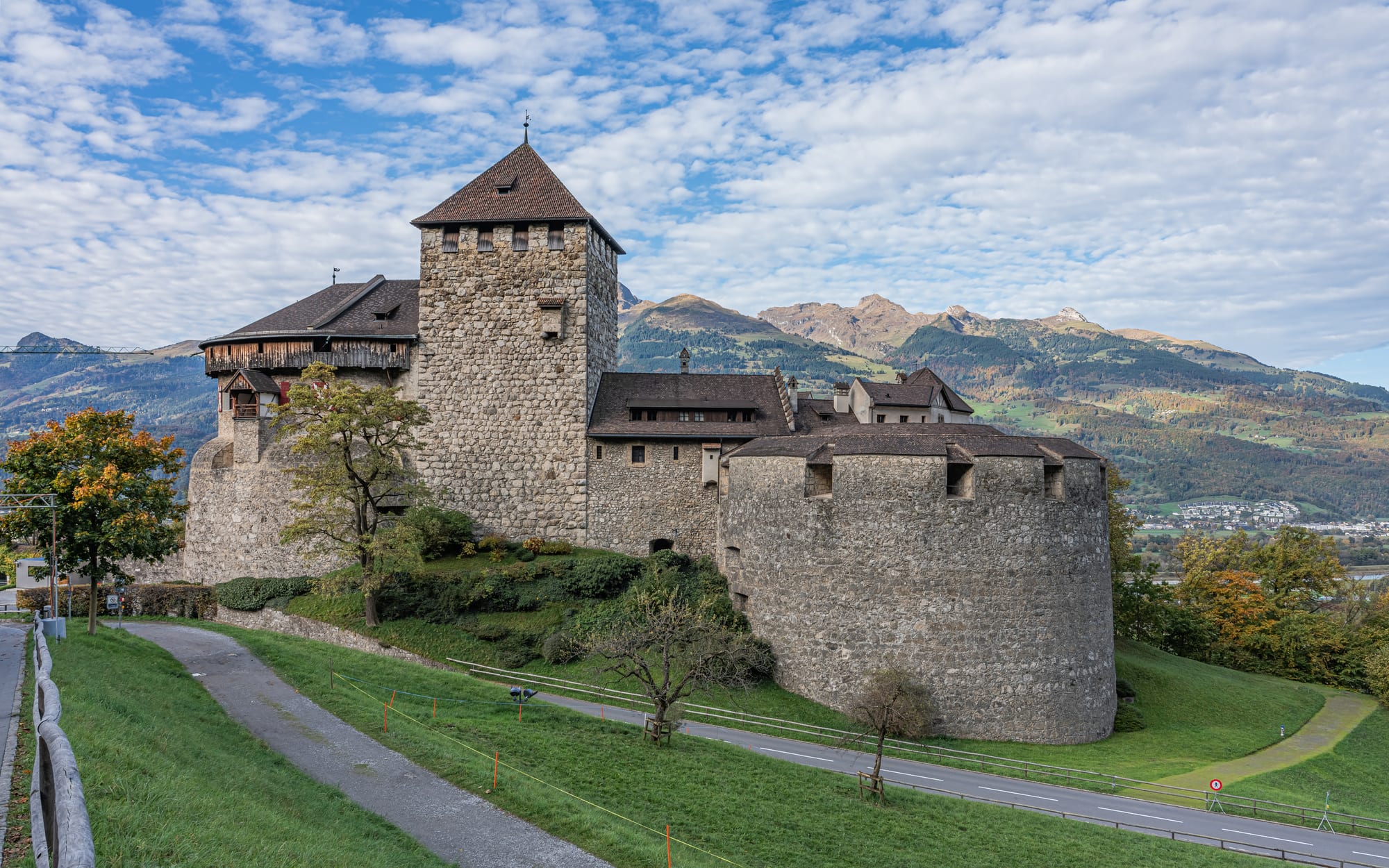 A cream-and-white medieval castle on a wooded hillside above a small town