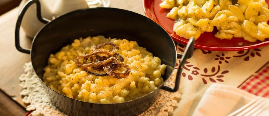 A dish of small dumplings covered in melted cheese and topped with fried onions
