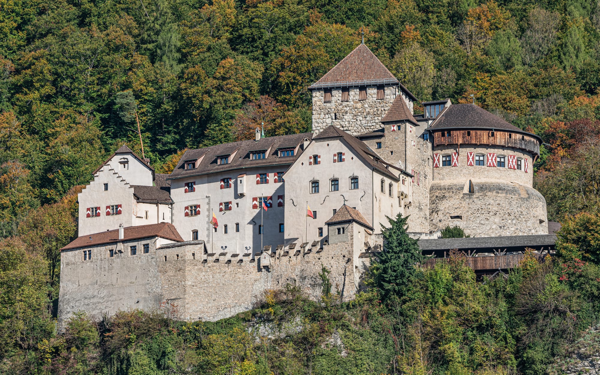 A medieval hillside castle with towers and a keep, overlooking a valley town and mountains