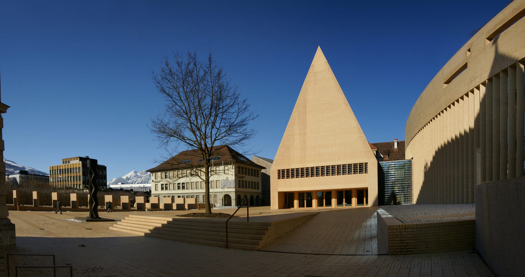 A modern brick parliament building with a steep pointed roof beside older buildings in Vaduz