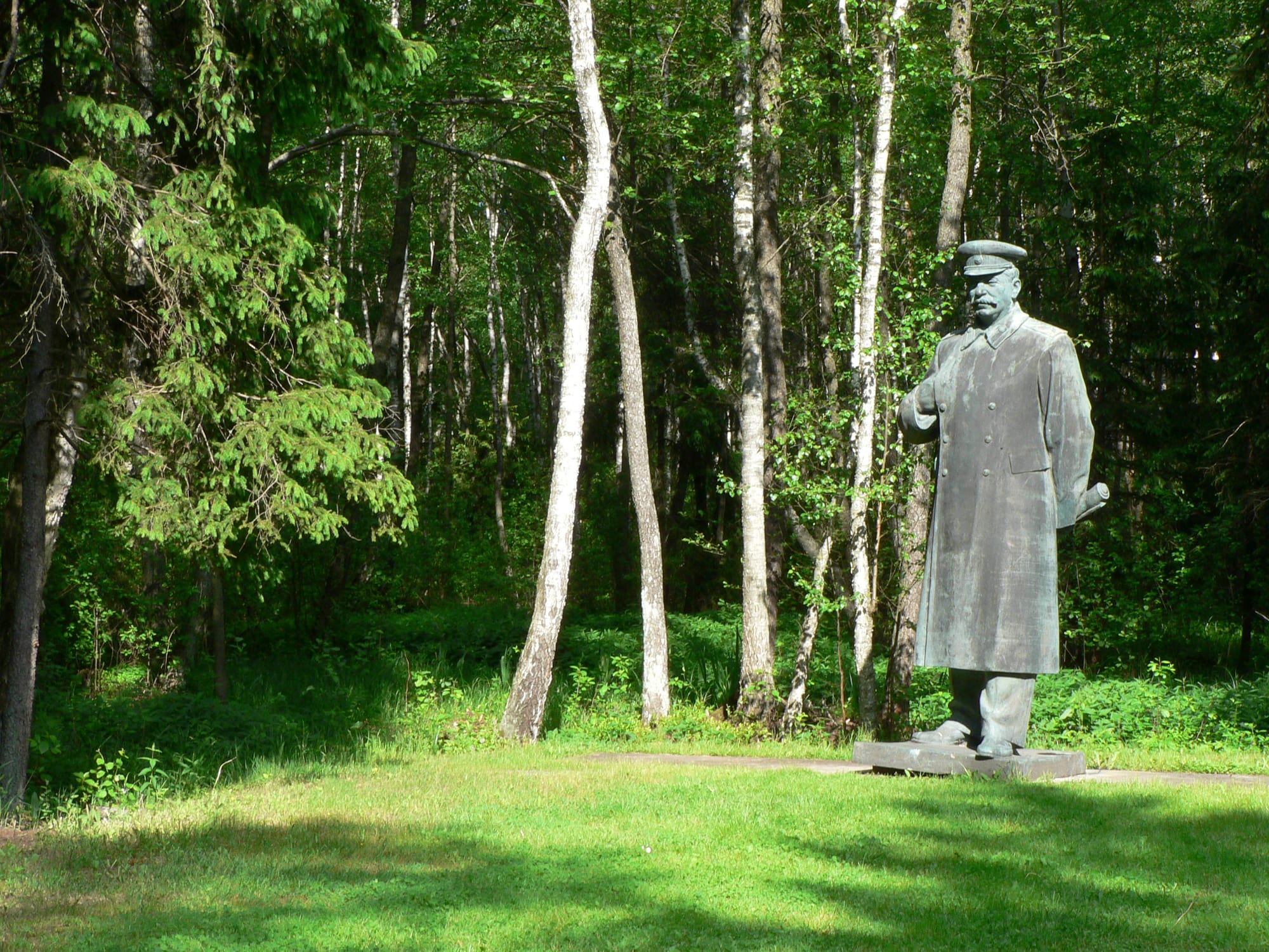 A large bronze statue of Stalin standing among trees in an outdoor park