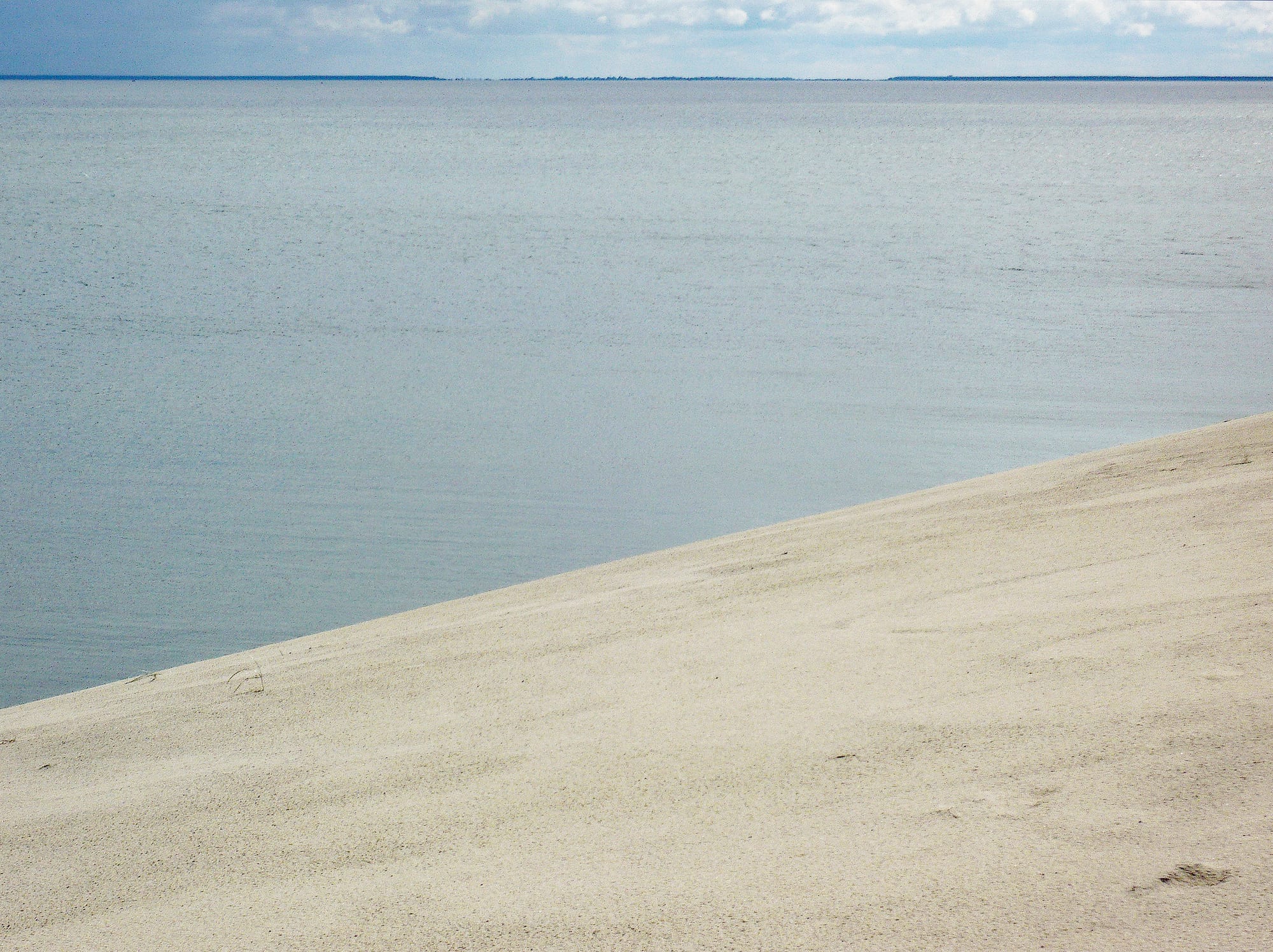 A high sand dune with sparse grass overlooking a calm lagoon