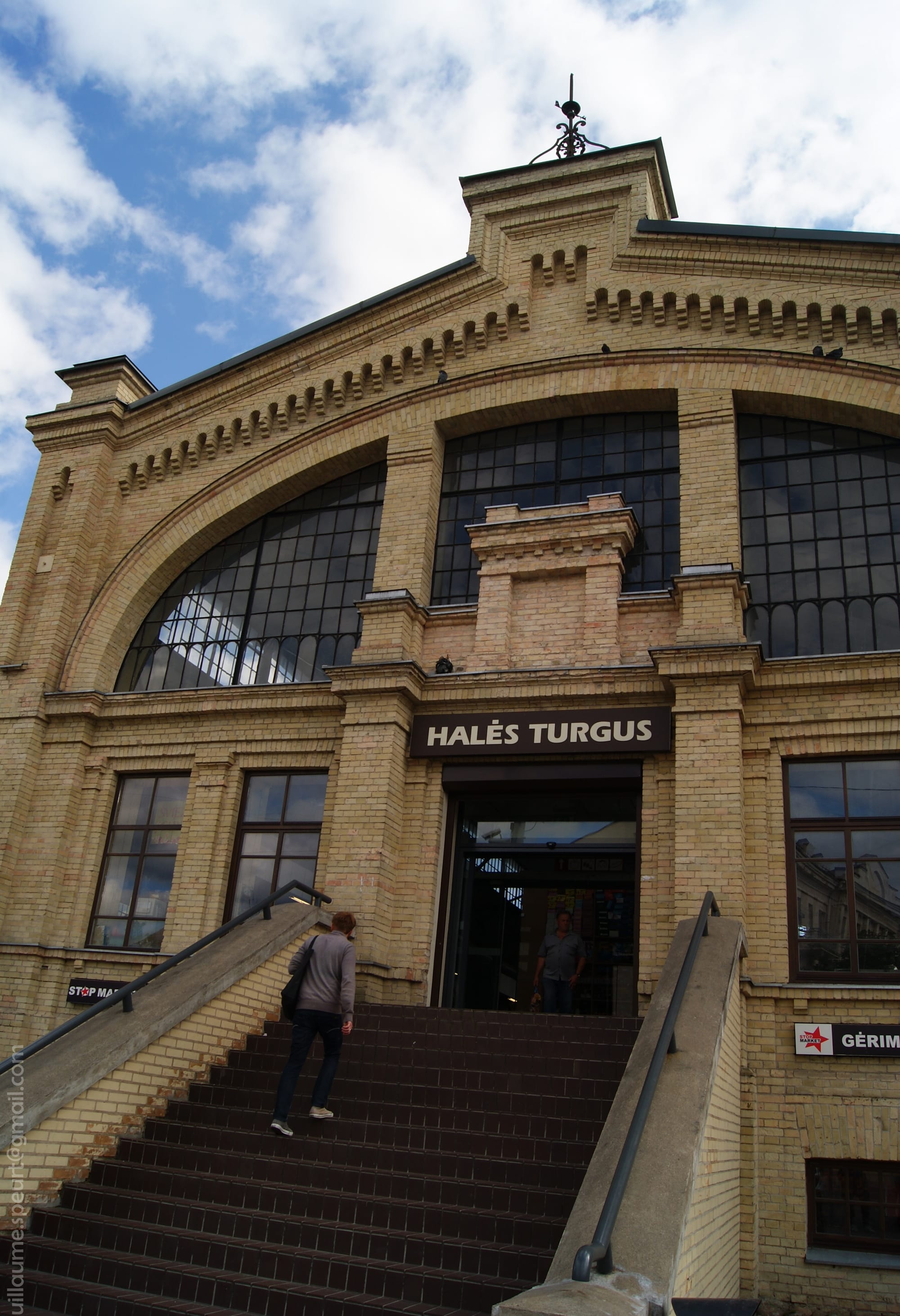 The brick facade and entrance staircase of a market hall, with a person walking up the steps