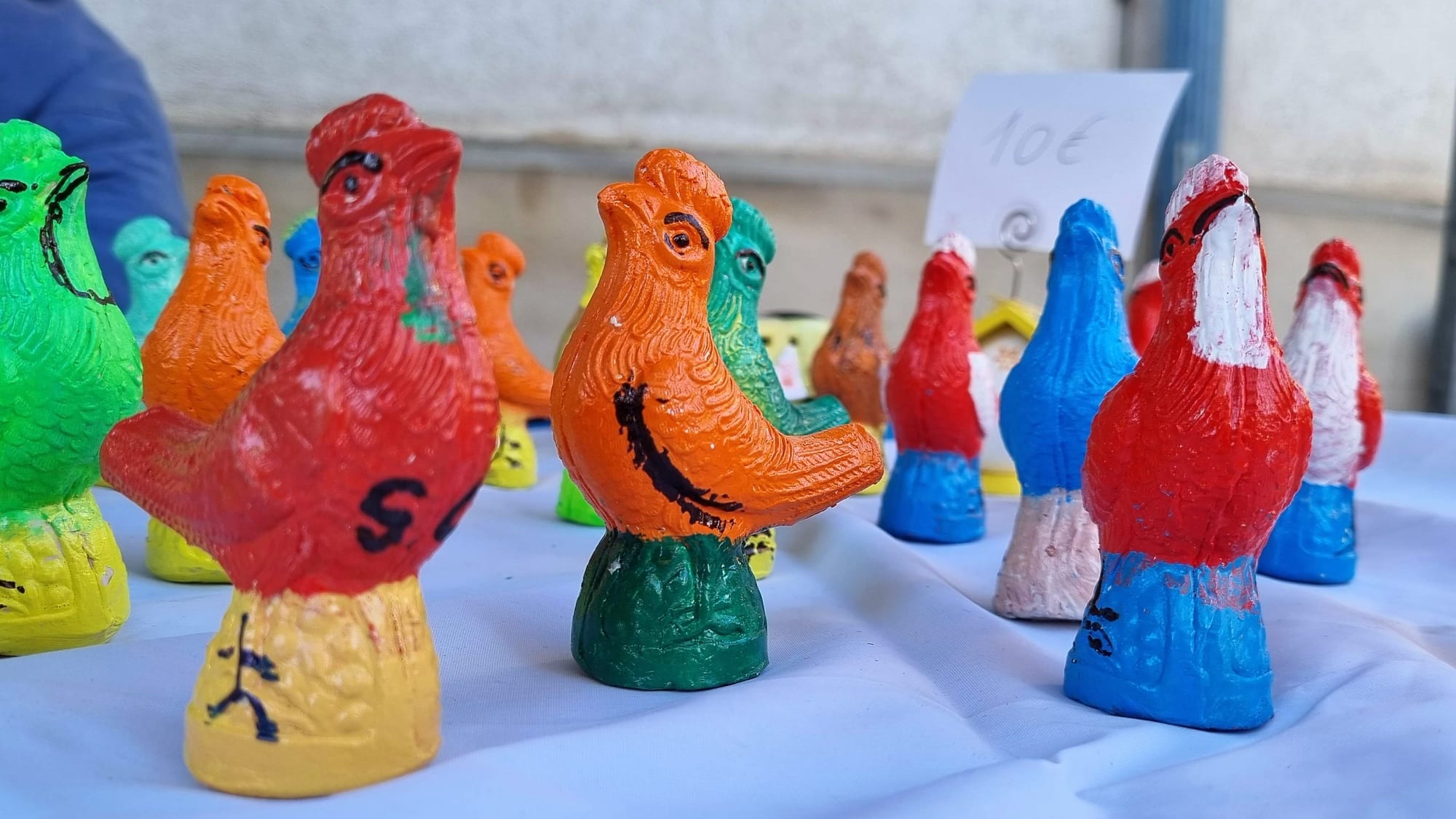 Rows of small terracotta bird whistles painted in bright red, orange, green and blue standing on a white tablecloth at a market stall