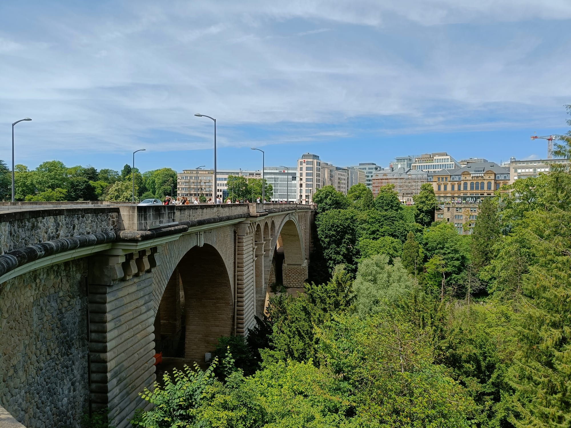 A large stone arch bridge spanning a deep green valley, city buildings on both sides