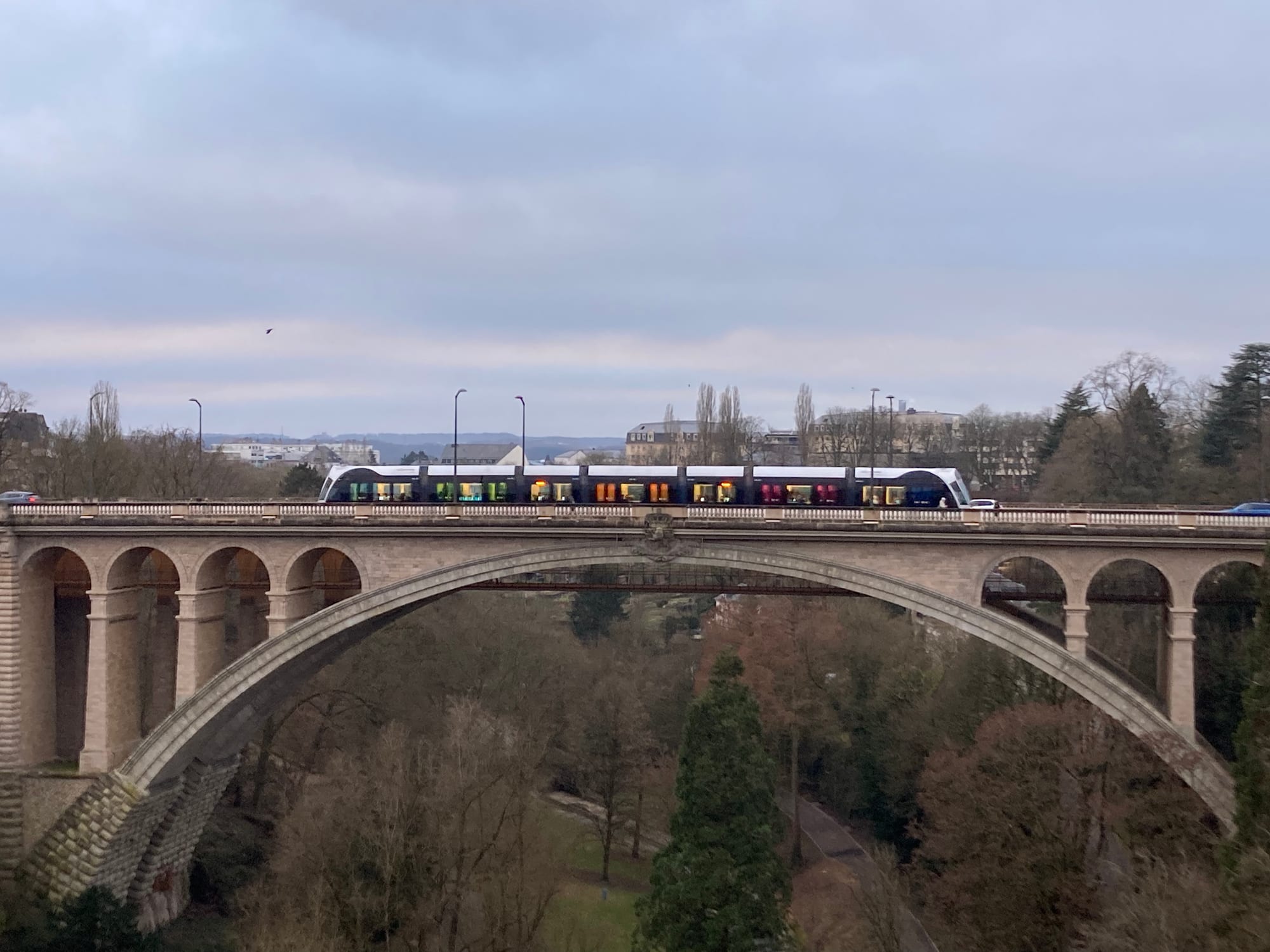 A tram crossing a tall stone road bridge in Luxembourg City