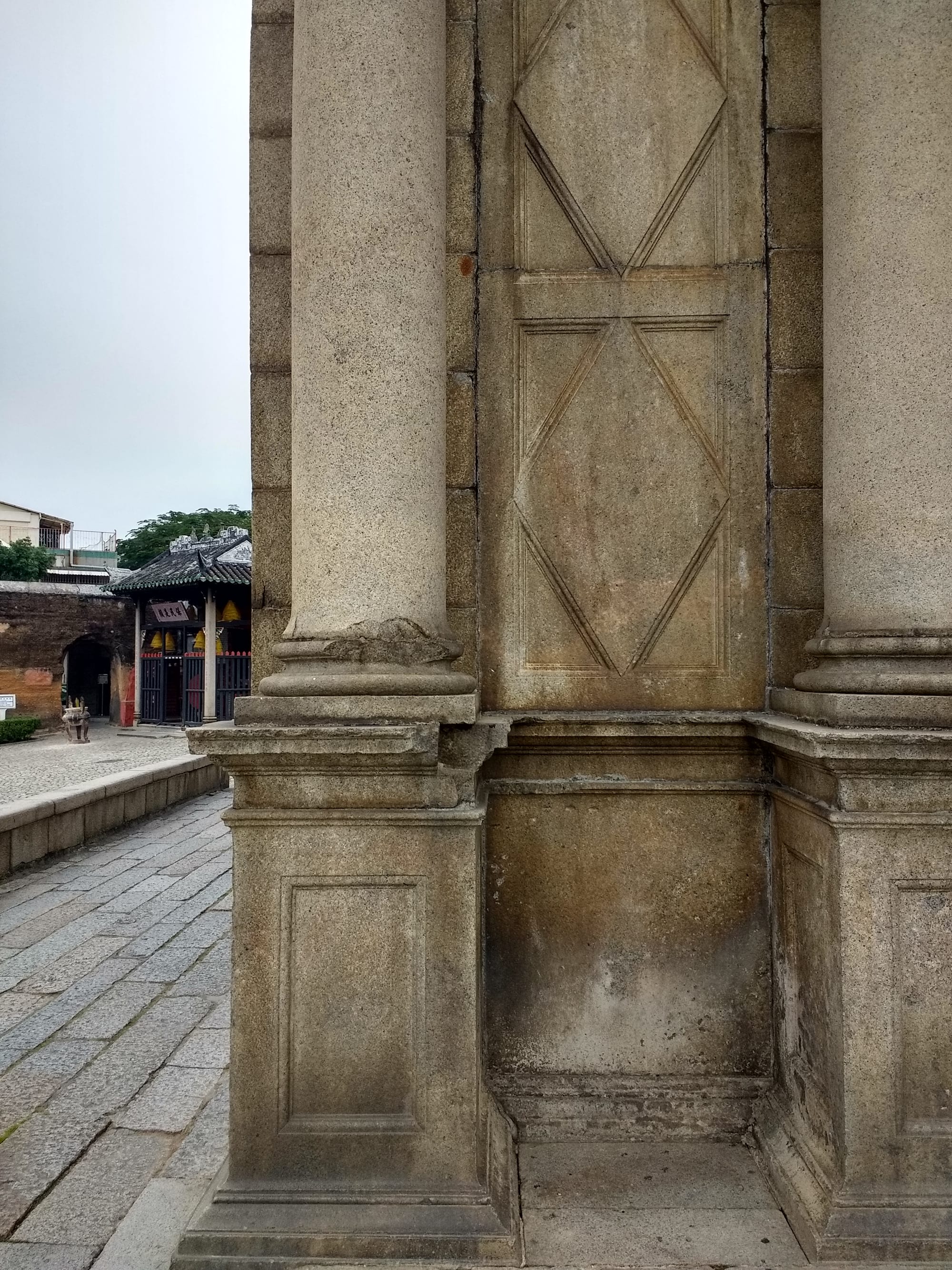 A tiny traditional Chinese temple standing right beside the tall ruined stone facade of a European church
