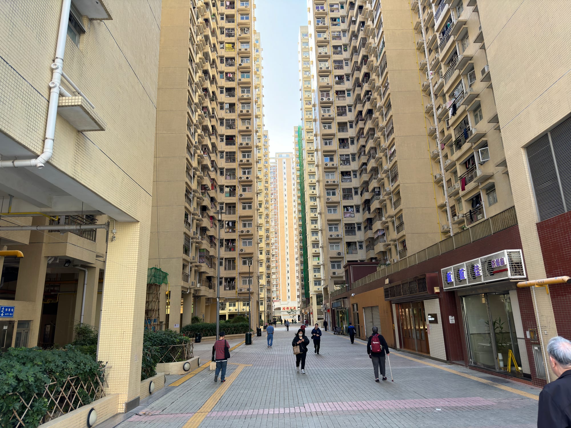 Very tall, closely packed residential tower blocks seen from a street below, with pedestrians walking between them