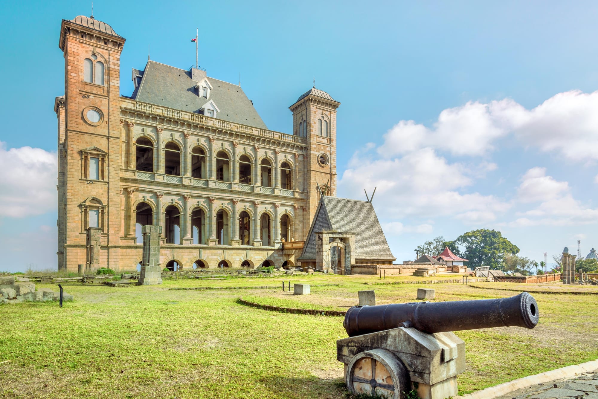 A tall dark stone palace complex with a steep roof on a hilltop above a city