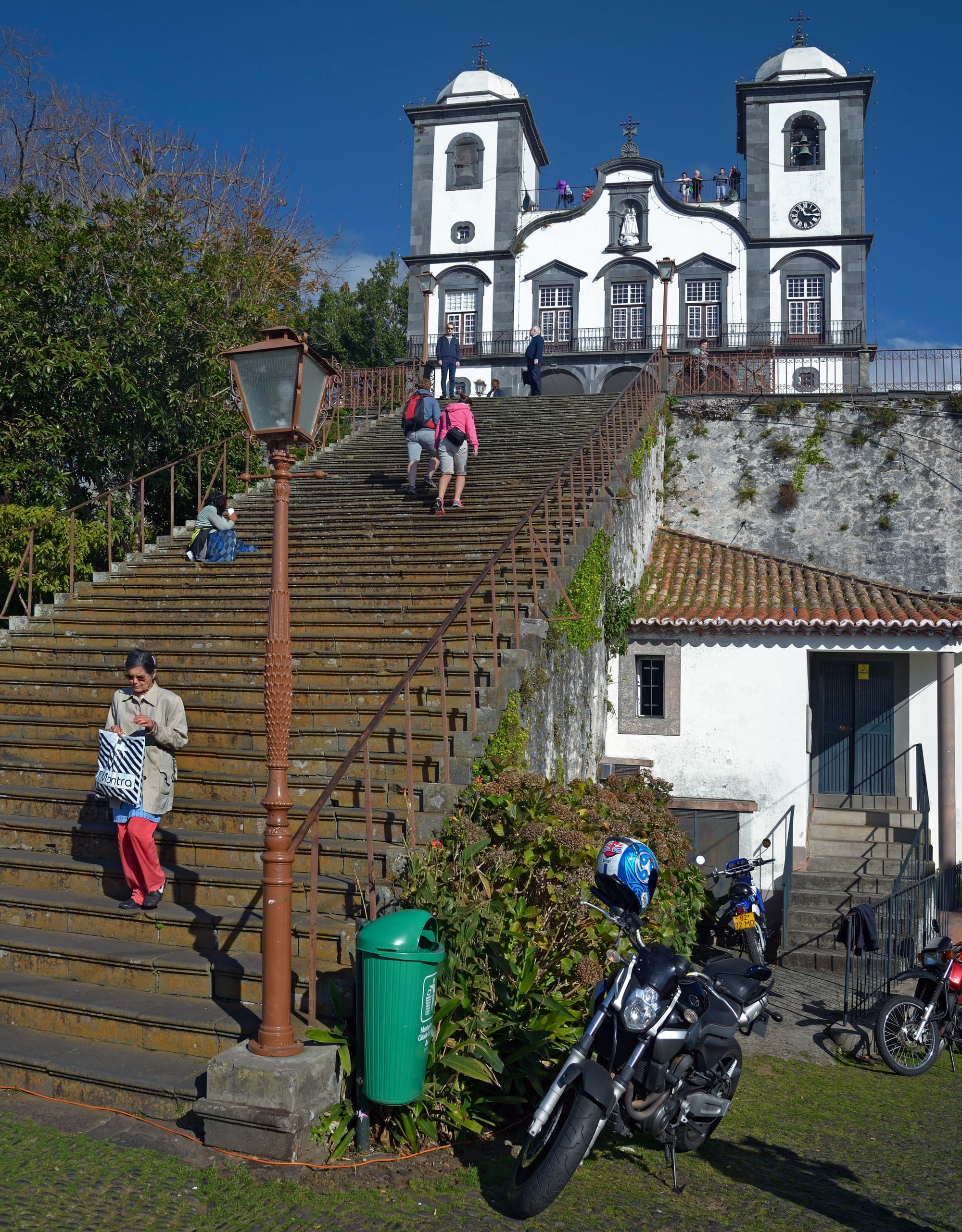 A long flight of stone steps with a metal handrail leads up to a white church with two bell towers and dark stone trim under a deep blue sky