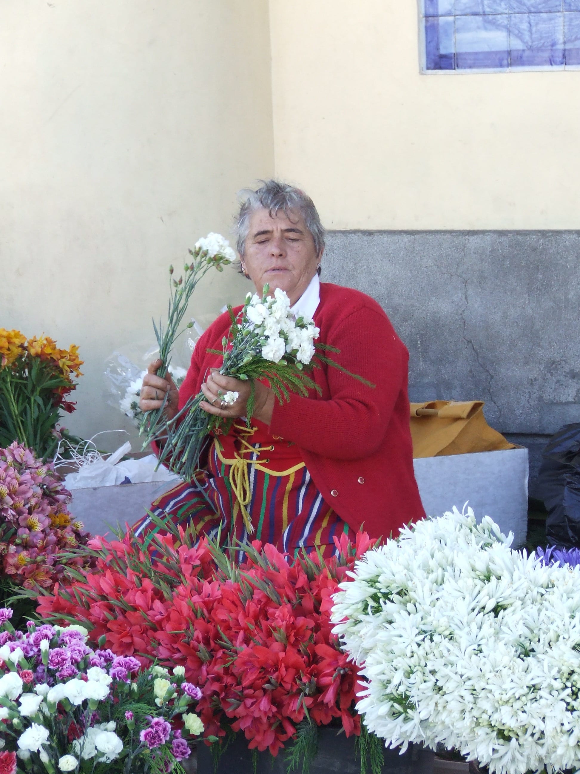 A woman in traditional dress arranging bunches of white and red flowers among market stalls at the Mercado dos Lavradores