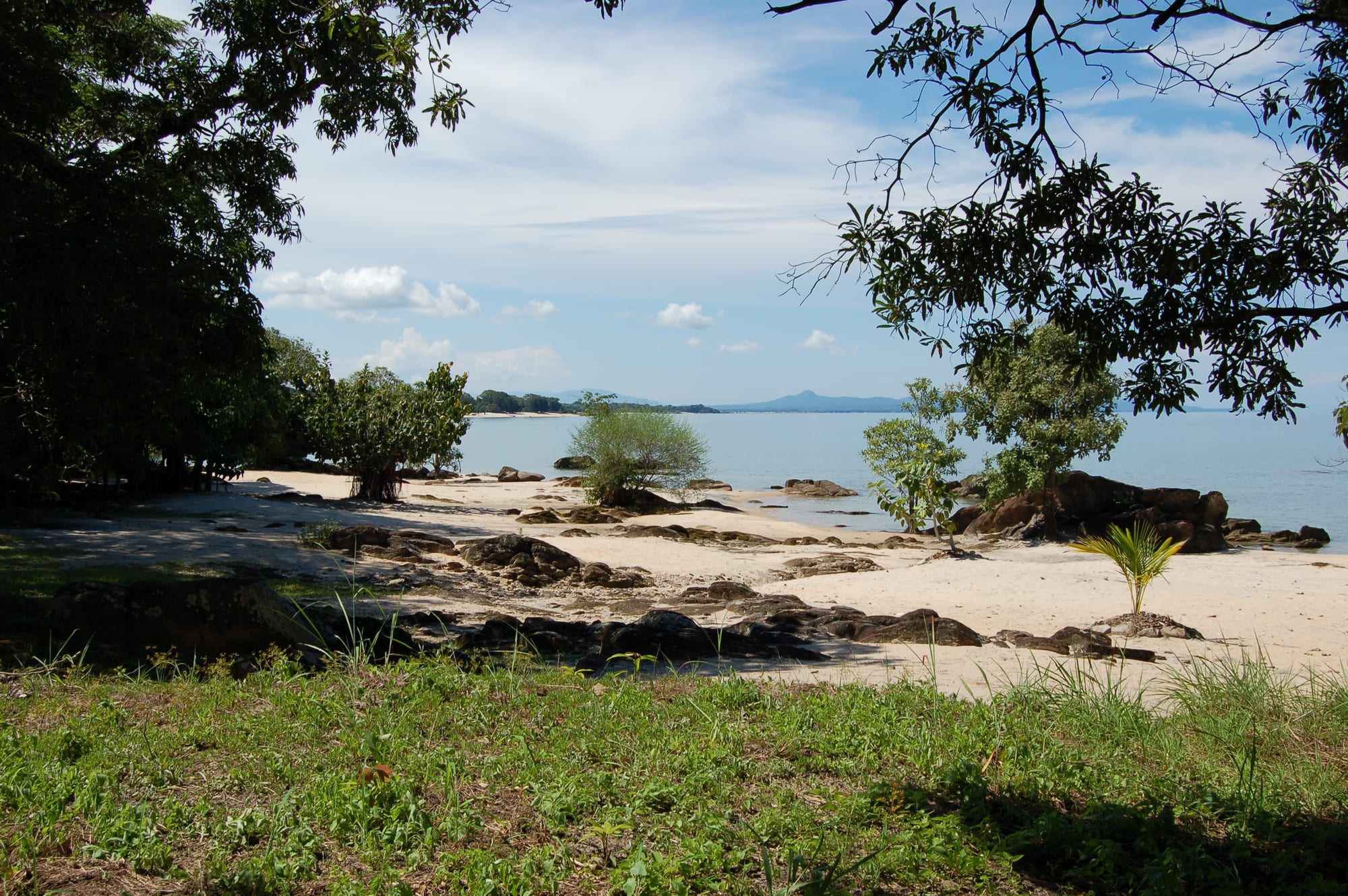 A calm freshwater lake with a sandy beach, fishing boats, and hills along the far shore
