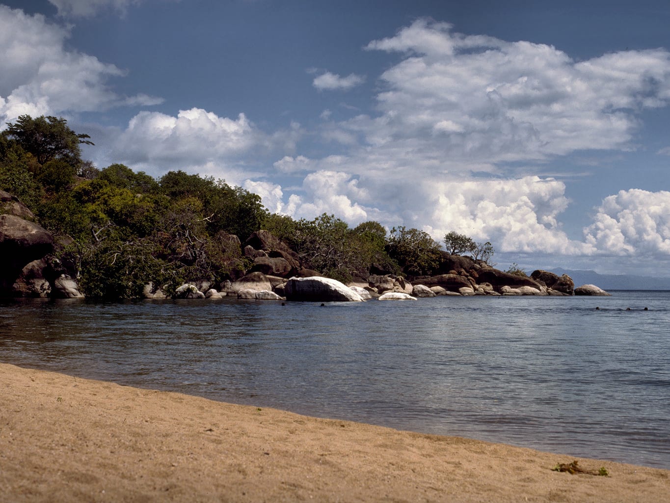 A rocky headland with clear turquoise water and small boats near a lakeside village