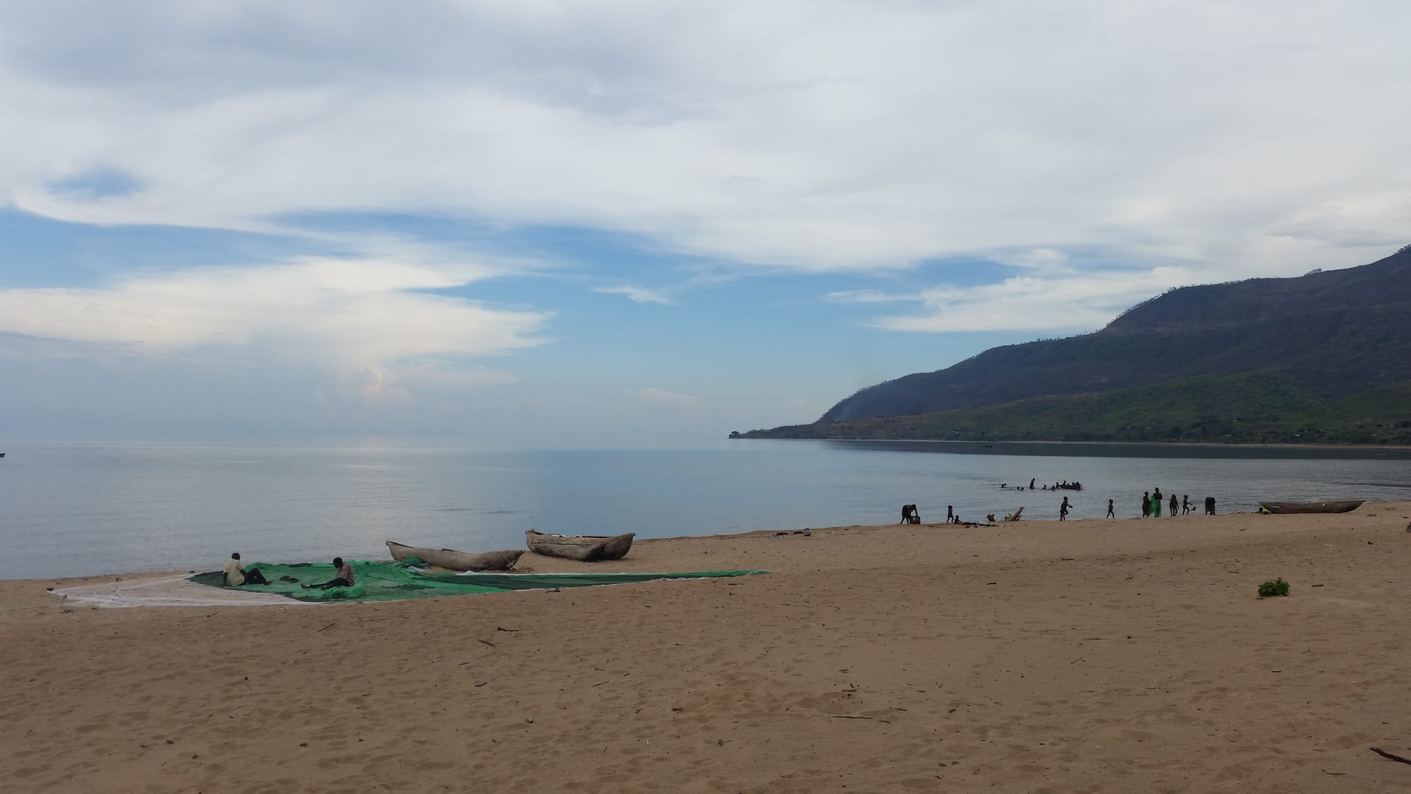 A sandy beach on Lake Malawi with dugout canoes pulled up on the shore and fishermen working with nets in the distance